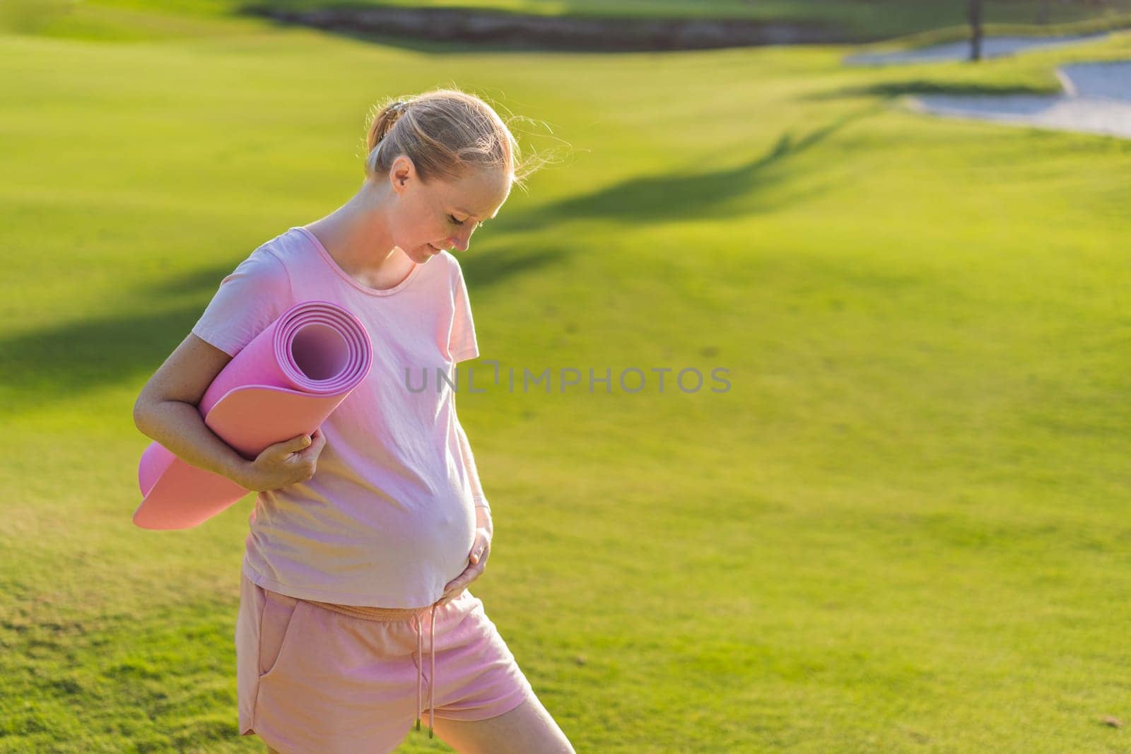 Energetic pregnant woman takes her workout outdoors, using an exercise mat for a refreshing and health-conscious outdoor exercise session by galitskaya