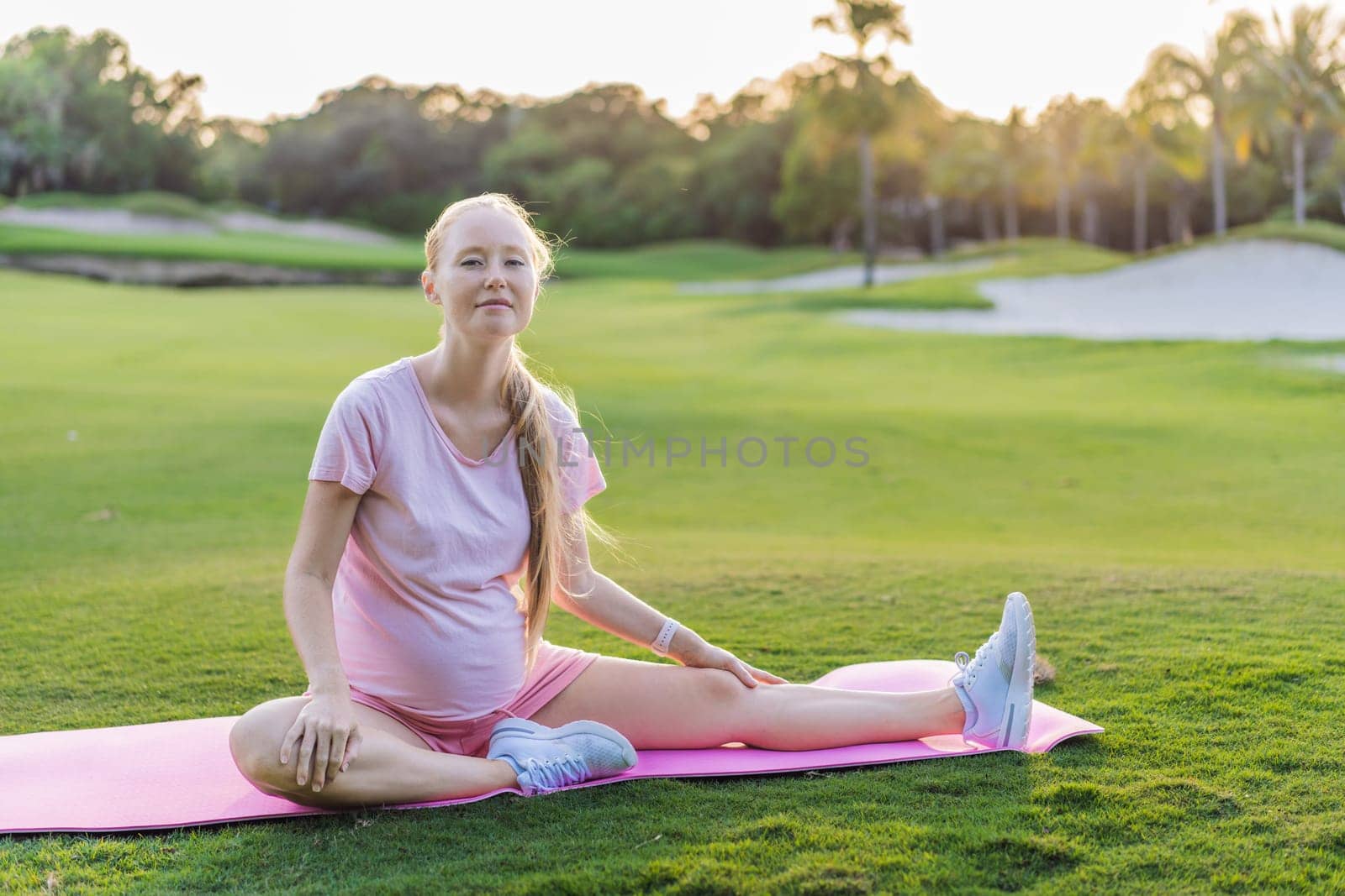 Energetic pregnant woman takes her workout outdoors, using an exercise mat for a refreshing and health-conscious outdoor exercise session by galitskaya