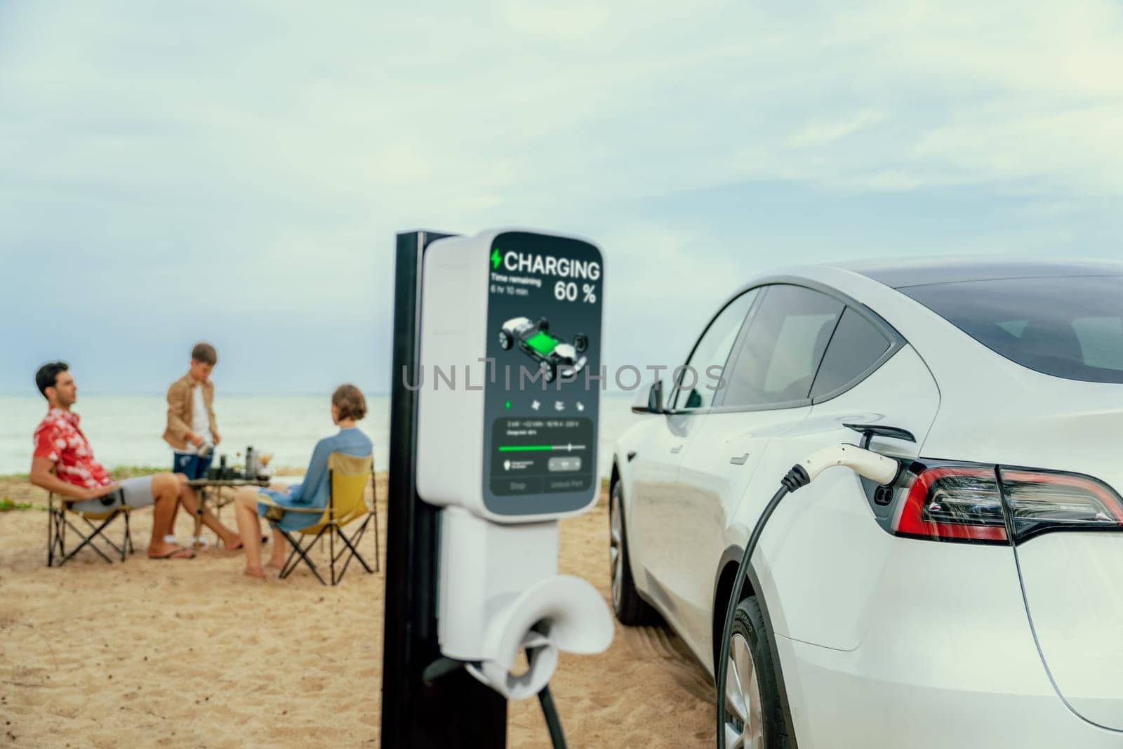 Alternative family vacation trip traveling by the beach with electric car recharging battery from EV charging station with blurred family enjoying the seascape background. Perpetual