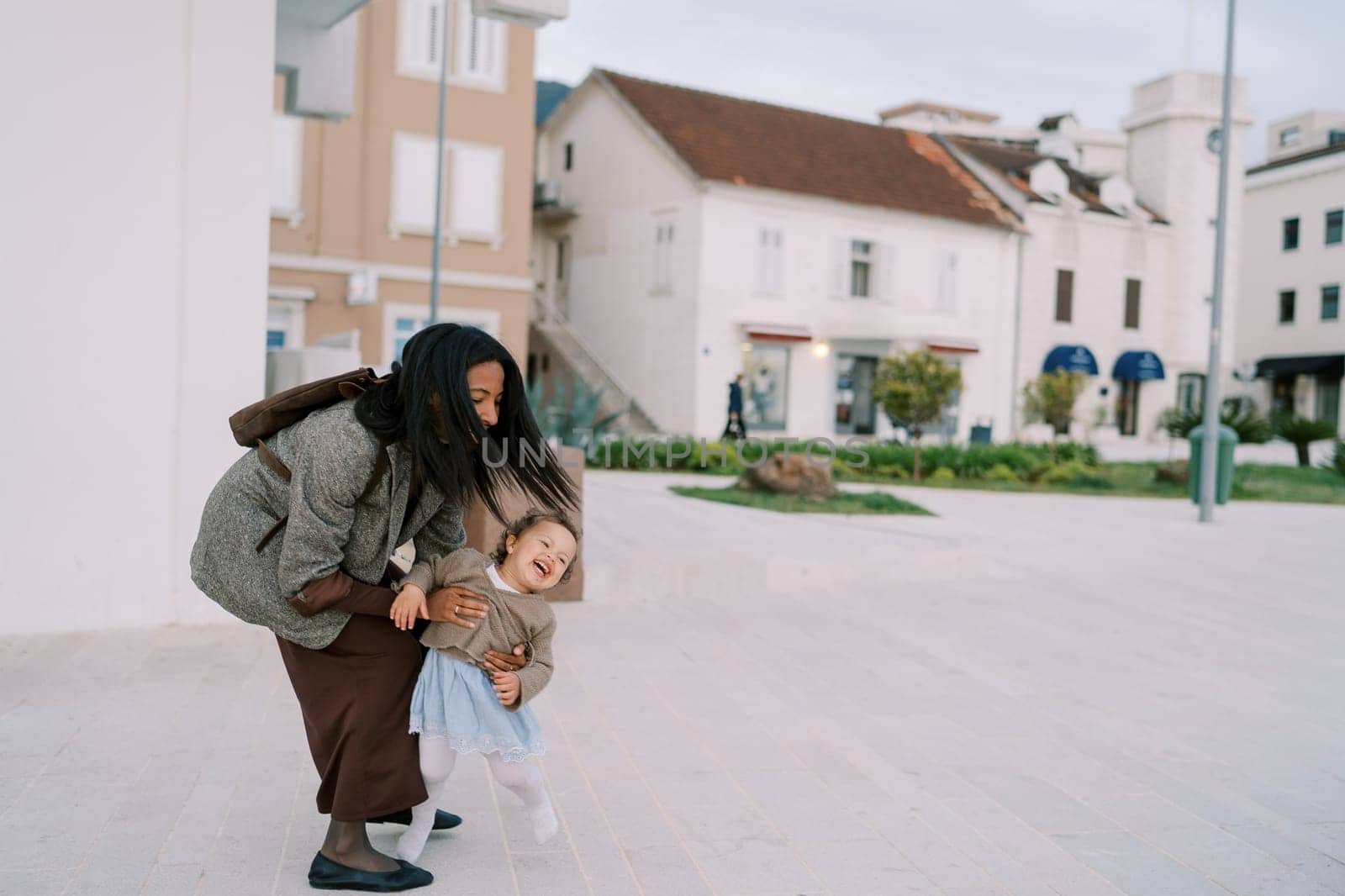 Smiling mother catches laughing little girl running near house. High quality photo