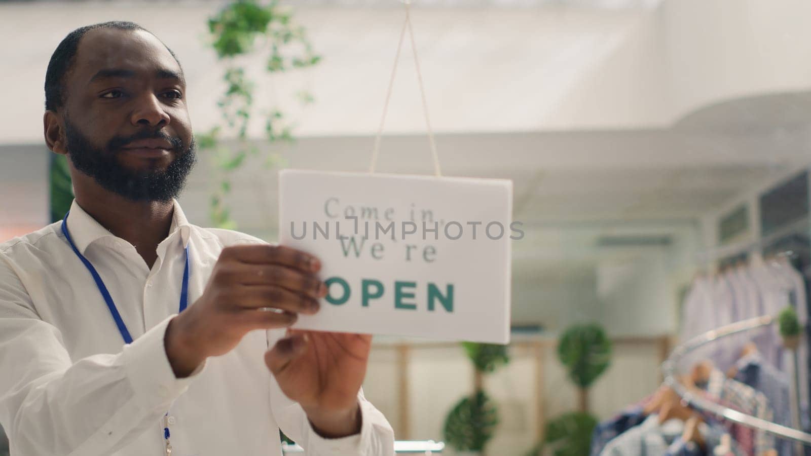 African american man opening fashion boutique business, starting shift in the morning. Smiling retailer turning closed sign on fast fashion clothing store into open one, close up shot