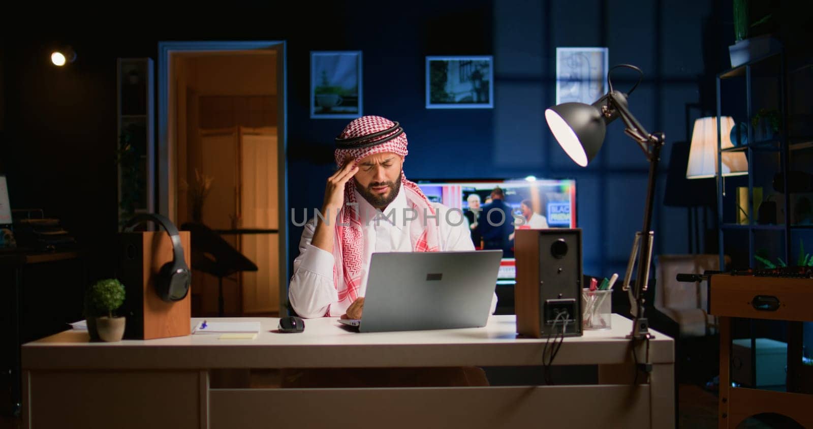 Tired arab businessman suffering migraine working at home office desk. Exhausted Middle Eastern employee in living room answering emails getting headache from overworking