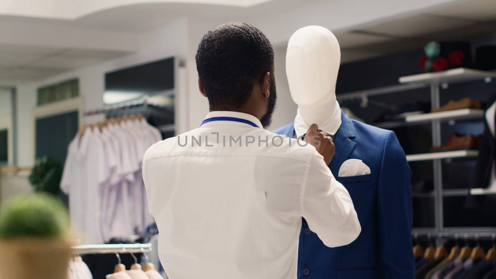 Employee tightening elegant blazer necktie on mannequin in luxurious clothing store. Worker arranging new collection stylish high class attire garments in premium fashion boutique
