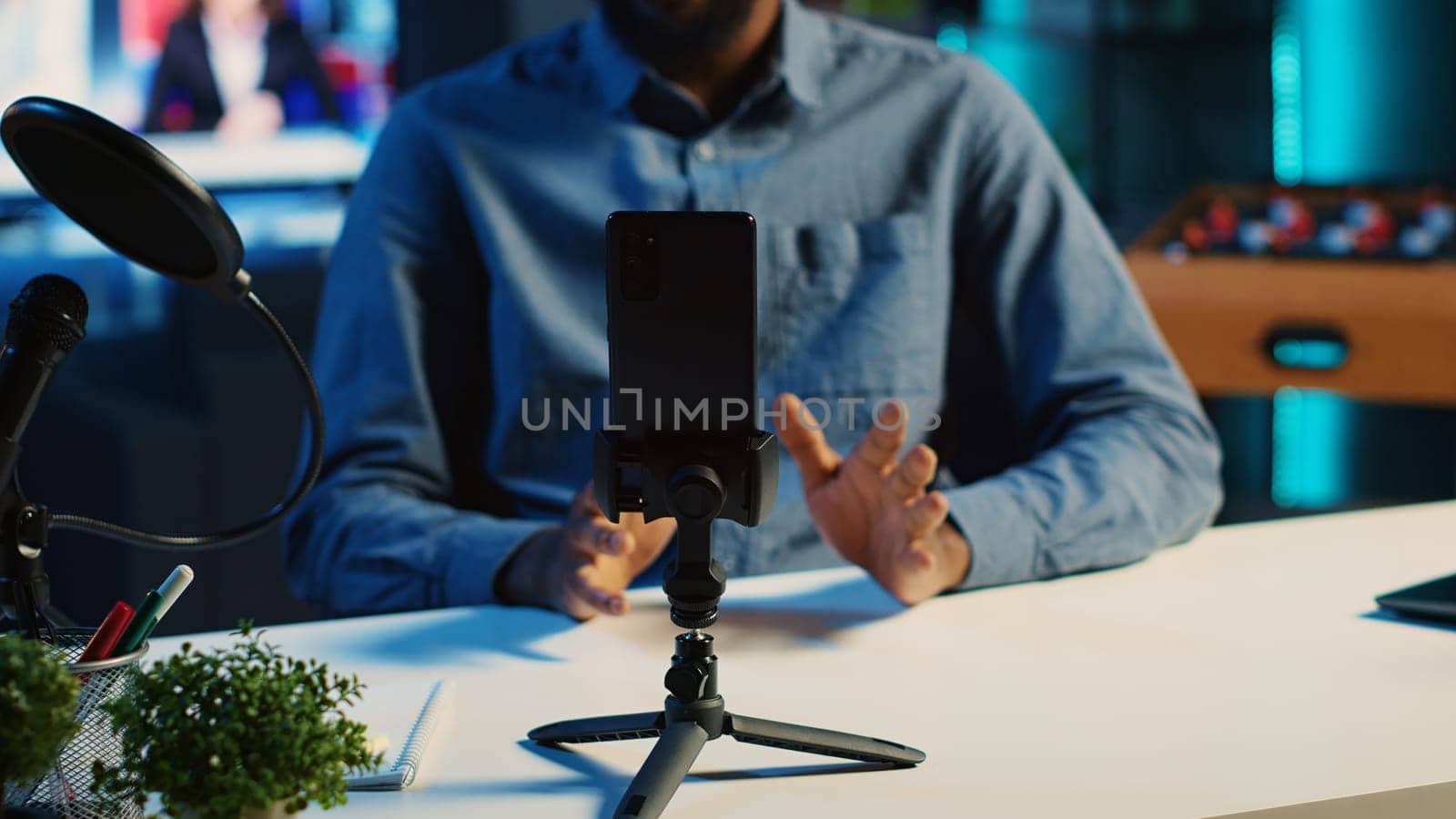 Close up shot of smartphone on holder used by content creator in dimly lit home studio to film video for online streaming platforms. Mobile phone being used by influencer to record footage