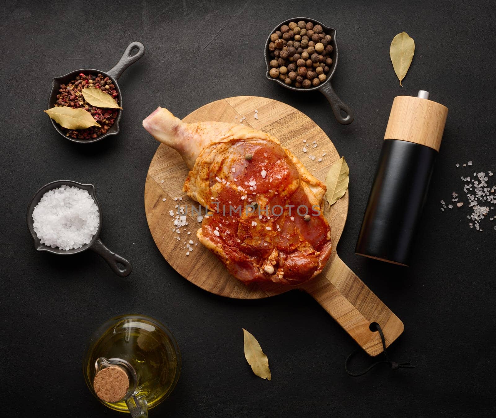 Raw chicken drumsticks seasoned on a wooden board, accompanied by salt and peppercorns, viewed from the top. Black table by ndanko