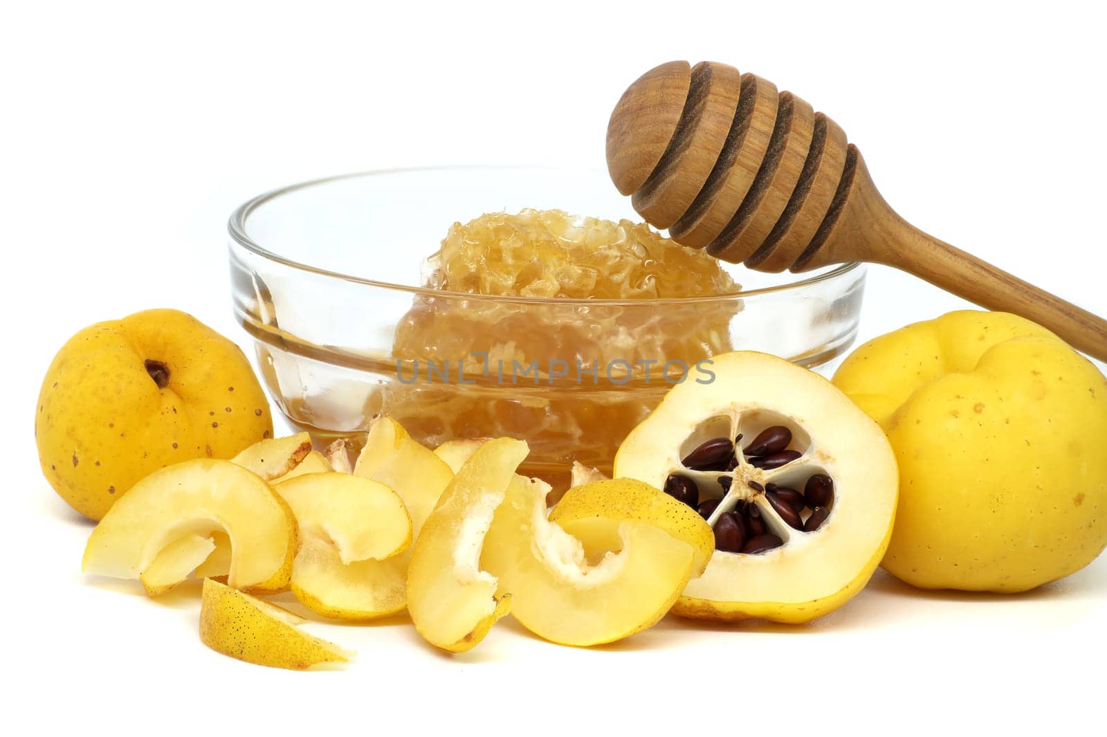 Glass bowl brimming with honey and wooden dipper resting on its rim surrounded by vibrant quince fruits, both sliced and whole isolated on white background, full depth of field