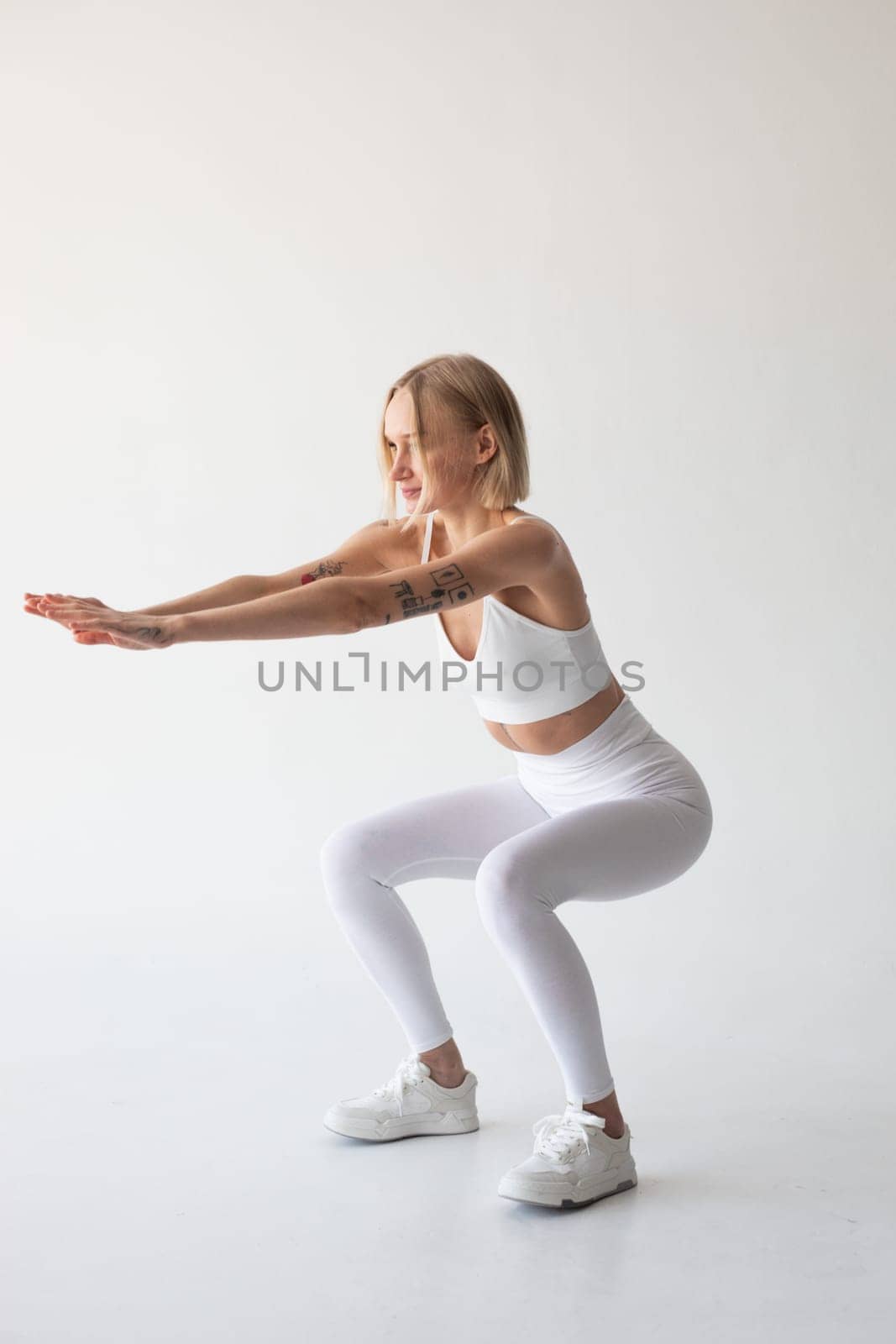 Beautiful blonde girl posing on a white background in white leggings and a white top by Freeman_Studio