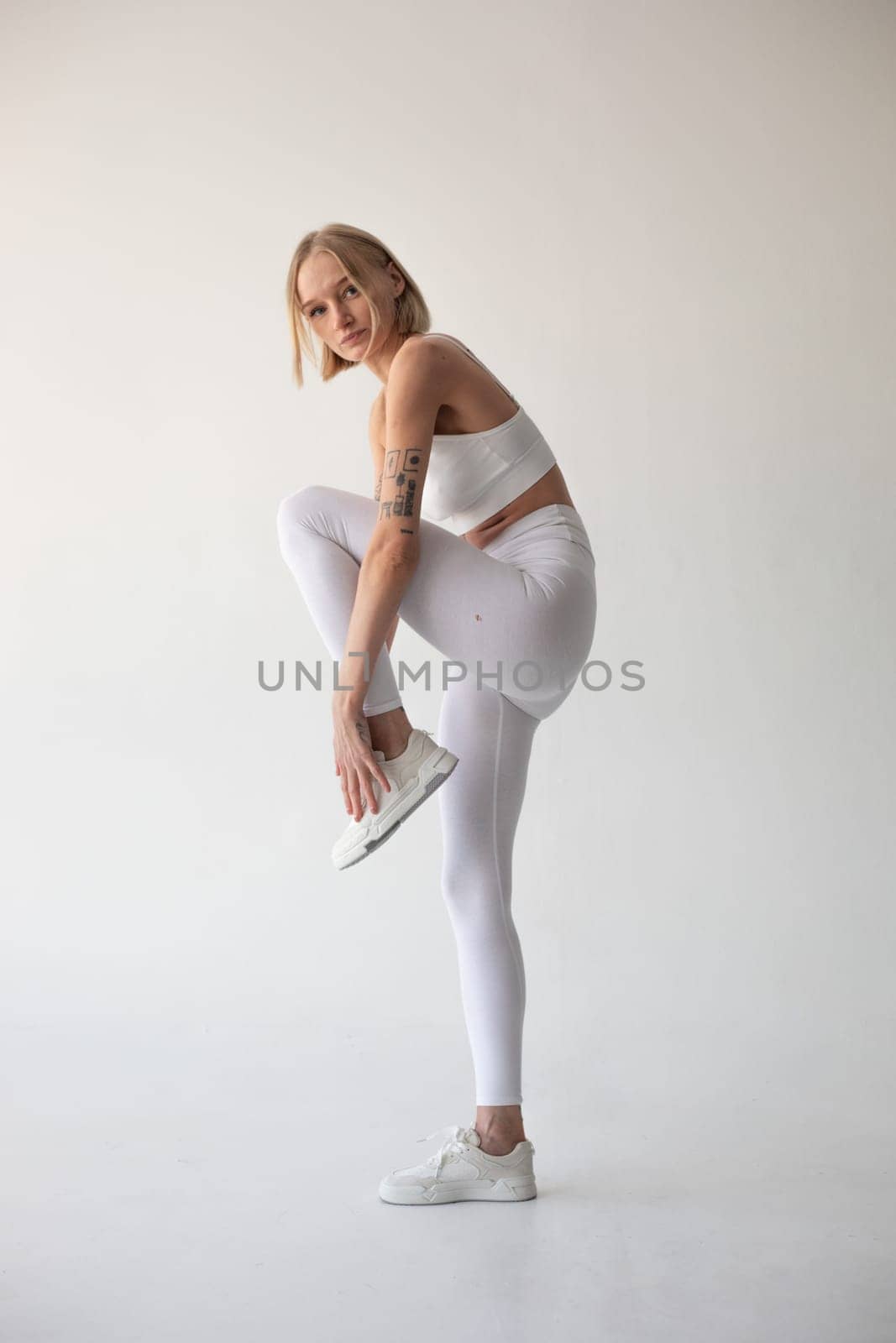 Beautiful blonde girl posing on a white background in white leggings and a white top by Freeman_Studio