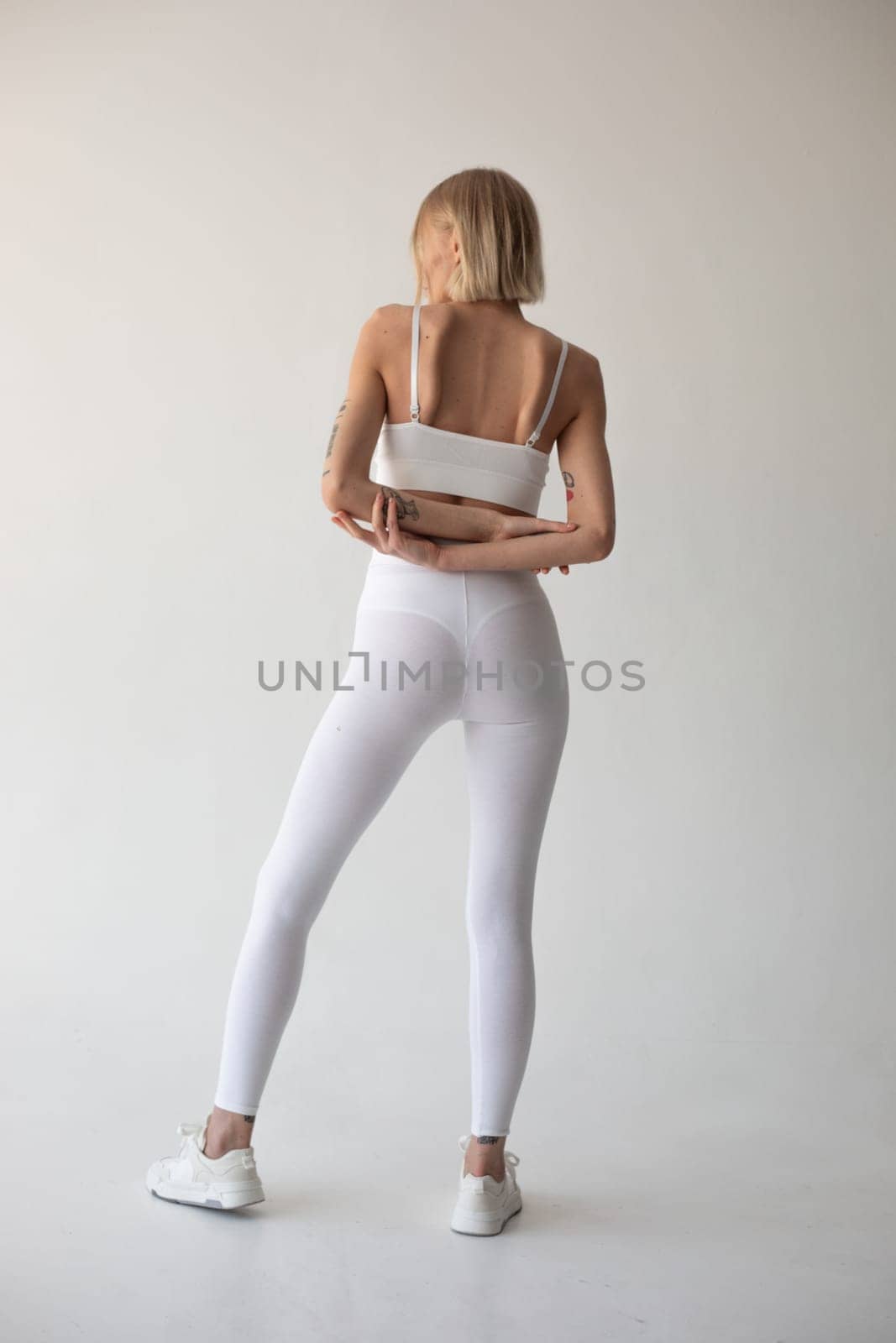 Beautiful blonde girl posing on a white background in white leggings and a white top. High quality photo