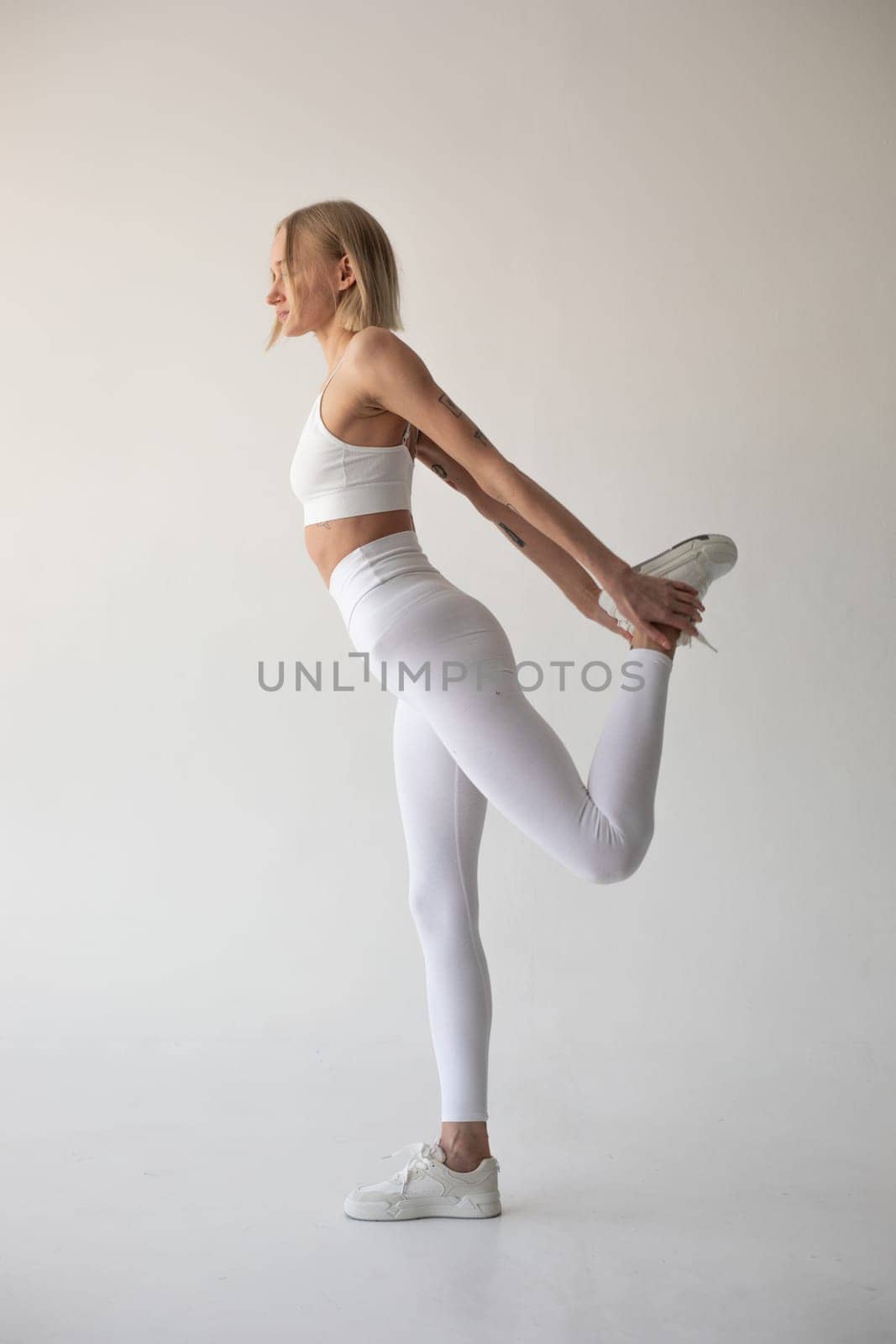 Beautiful blonde girl posing on a white background in white leggings and a white top. High quality photo