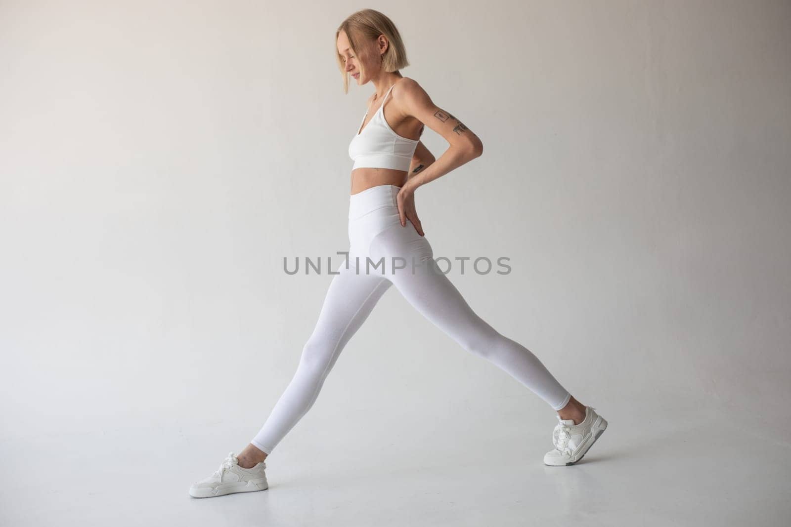 Beautiful blonde girl posing on a white background in white leggings and a white top. High quality photo