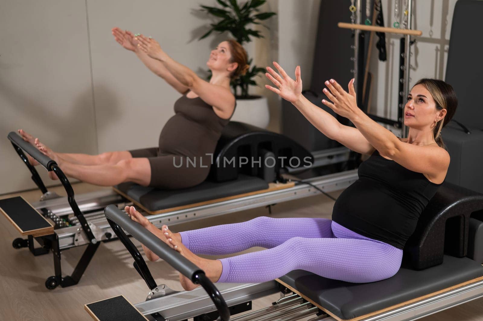 Two pregnant women do Pilates exercises on a reformer. Yoga class for pregnant women