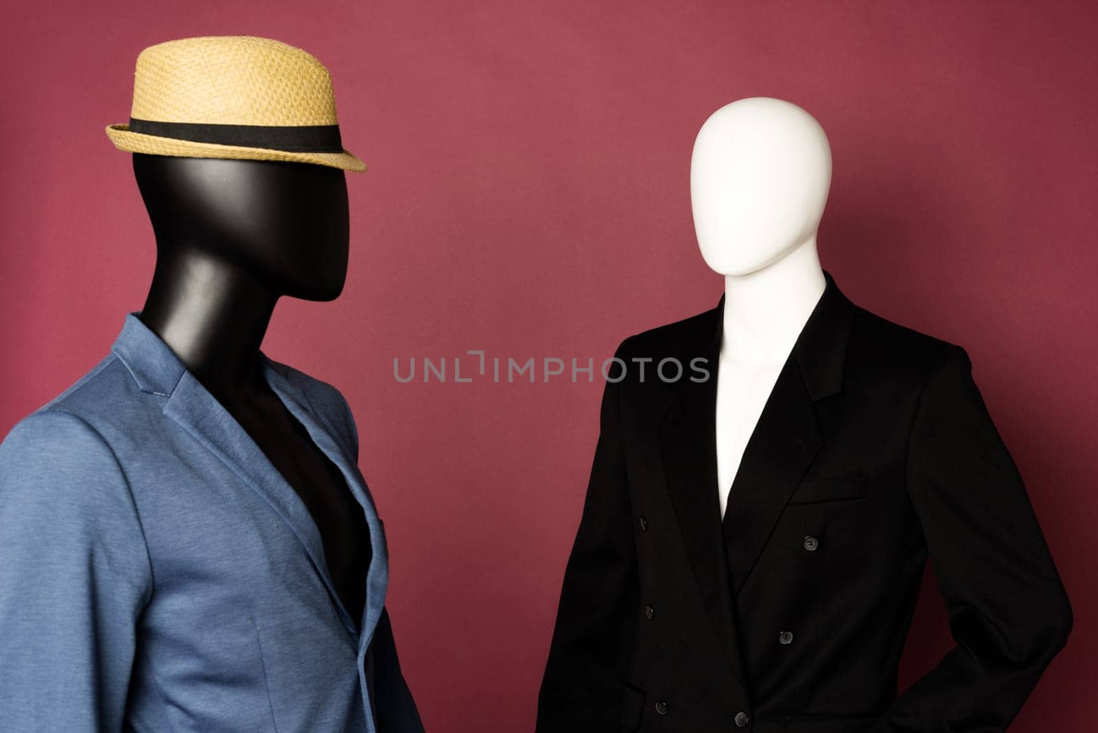 Two male mannequin in a black business suit and in a blue suit and white pants on a ruby background - image
