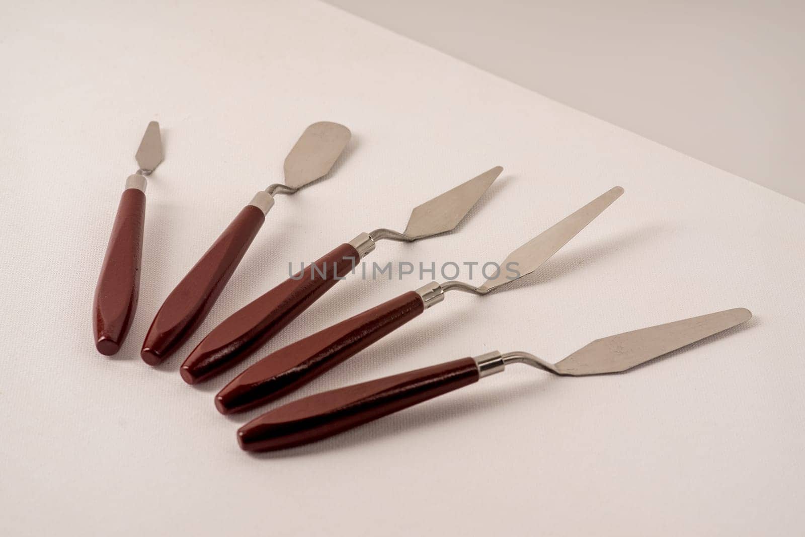 Five art palette knives lie on a white art canvas.