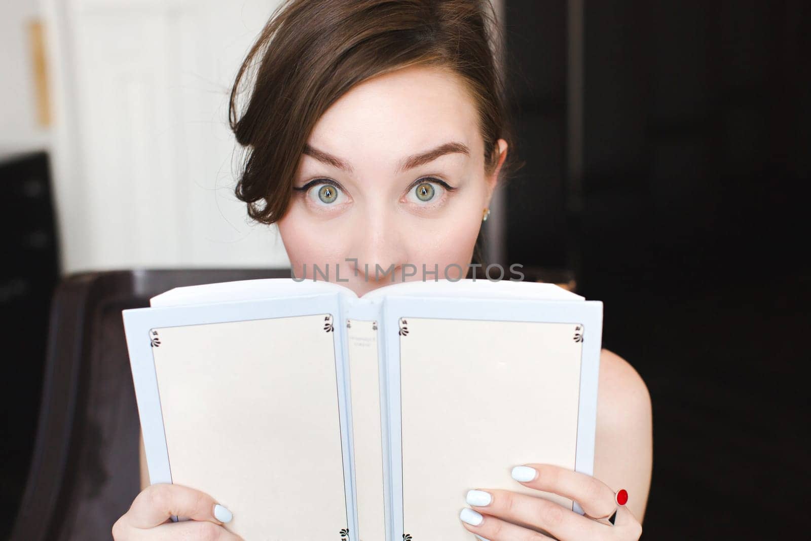 Woman hiding behind the grey book. Woman covering her face. Woman hiding face behind book looking at camera surprise. Education concept. Face expression. Girl holding book.