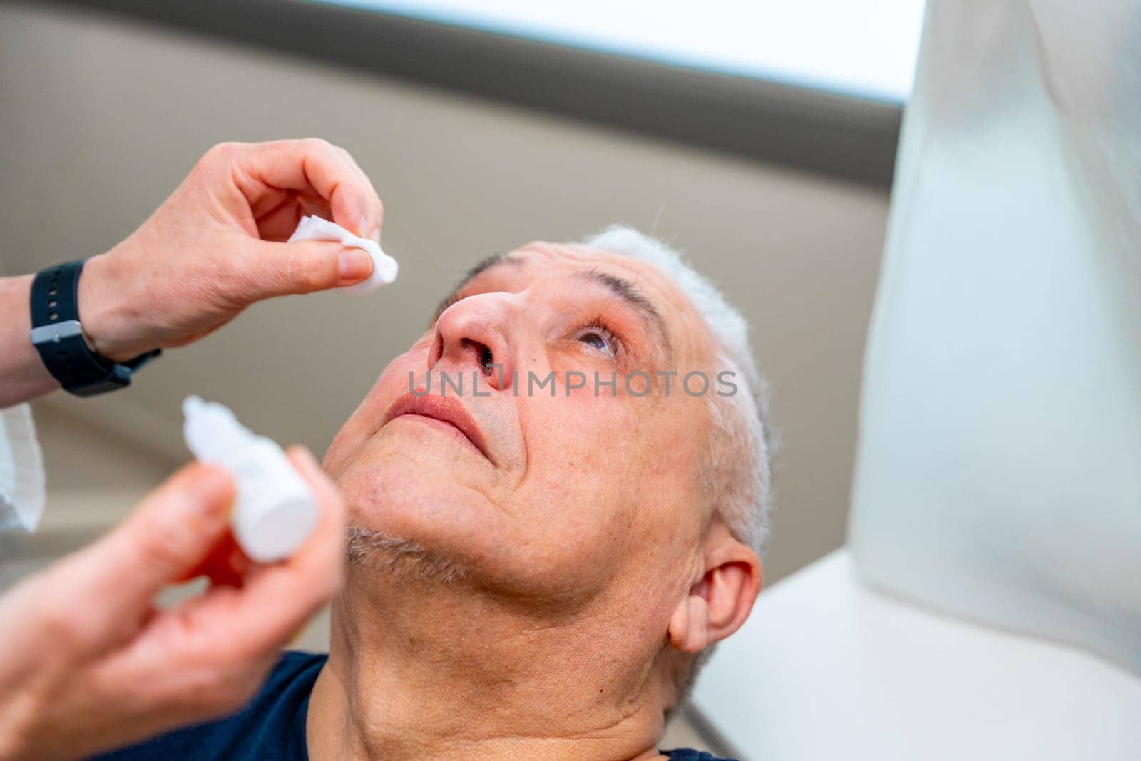 Ophthalmologist applies drops to dilate the pupil to a man by Huizi