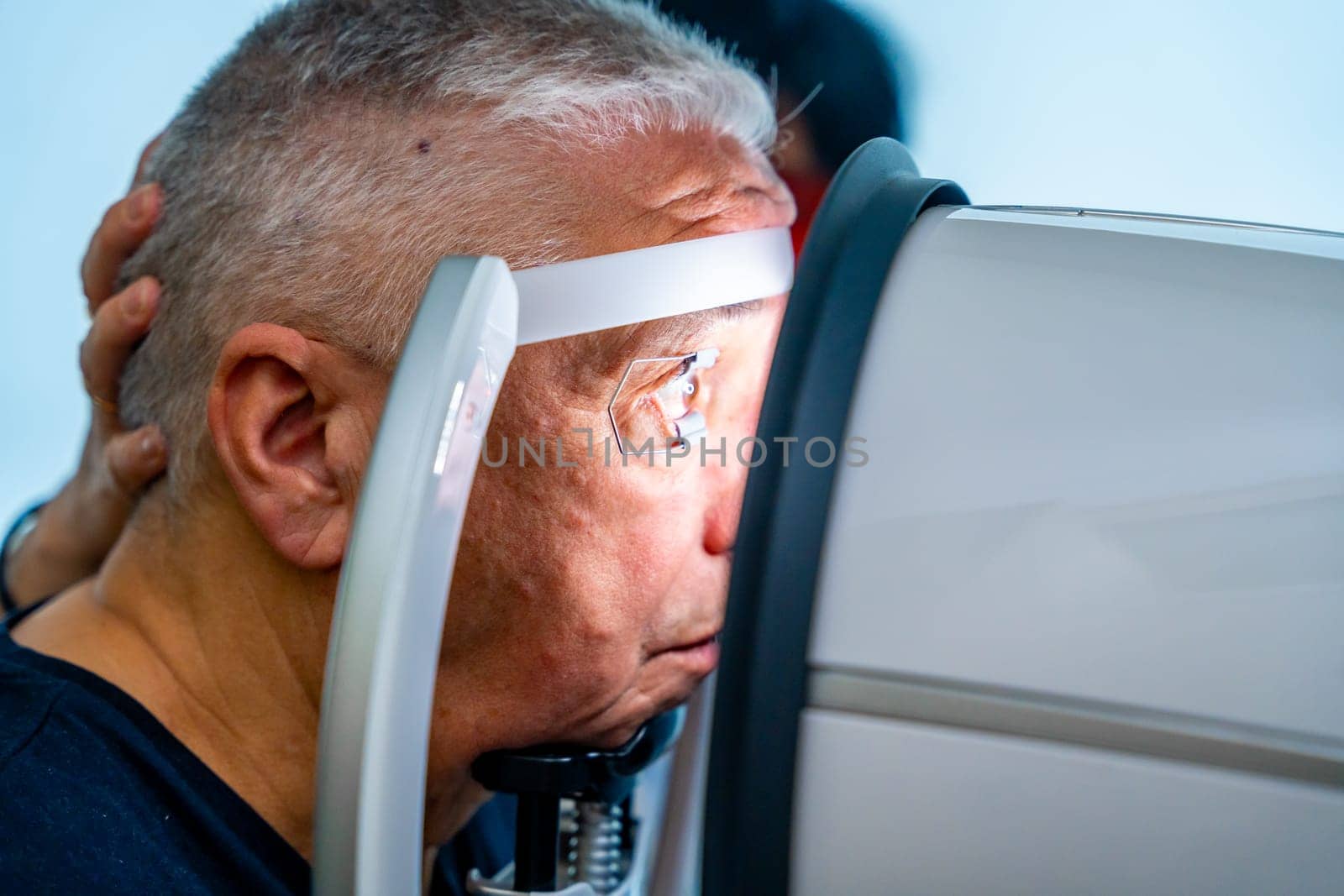 Senior man leaning the head on scanner to check glaucoma by Huizi