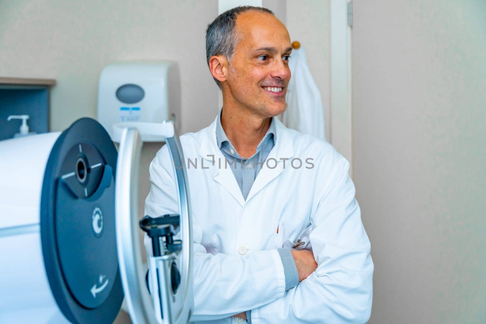 Proud mature male ophthalmologist looking distracted next to an innovative laser machine in a clinic
