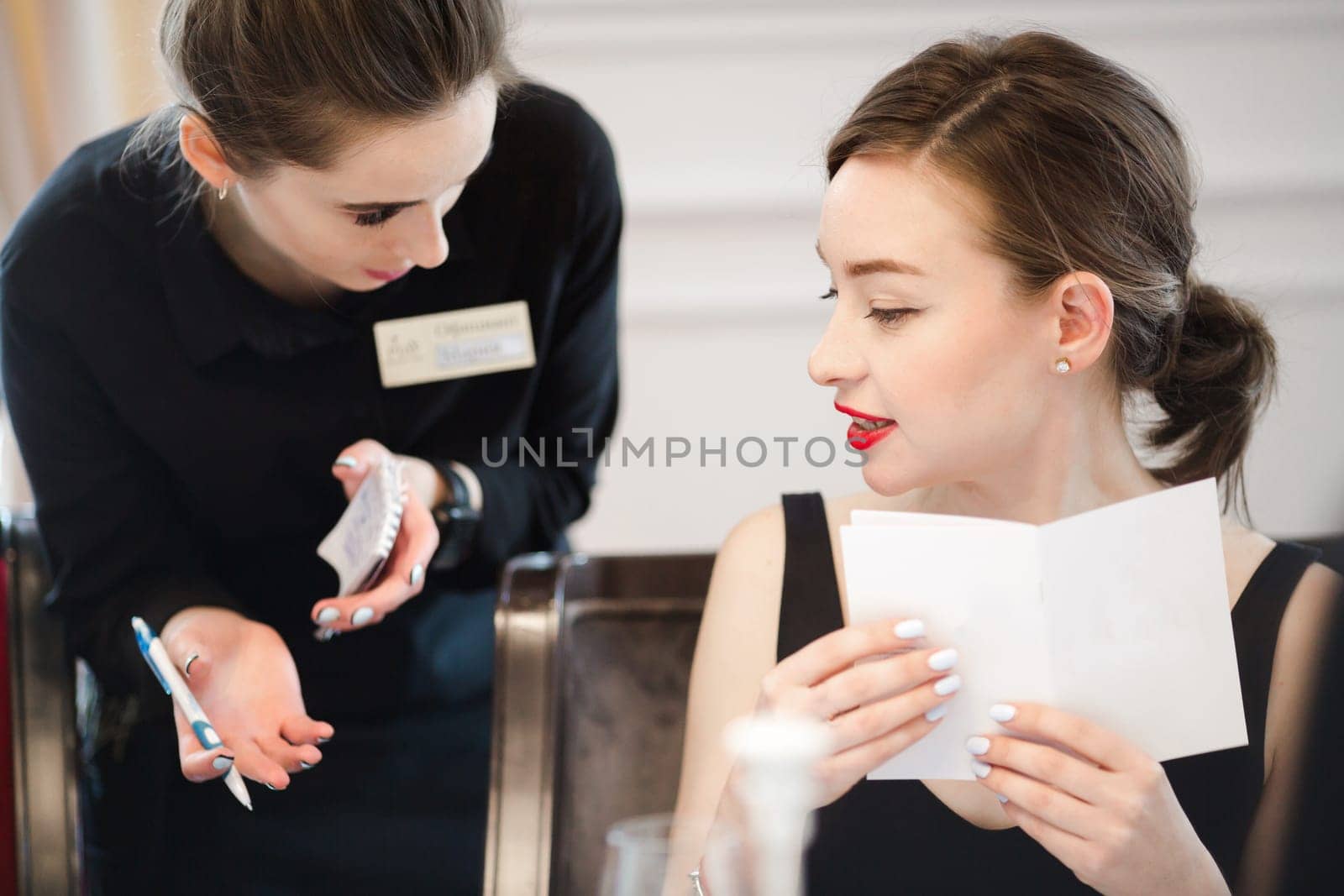 Woman making an order from the waitress menu. Smiling waitress taking an order in cafe