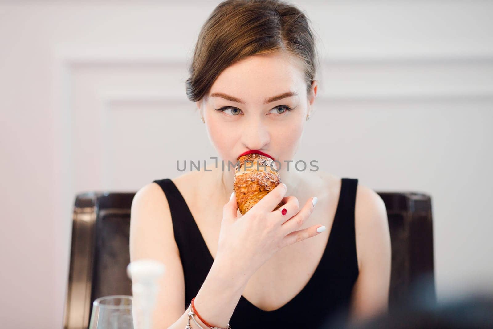 Made-up woman biting in a croissant in a cafe interior