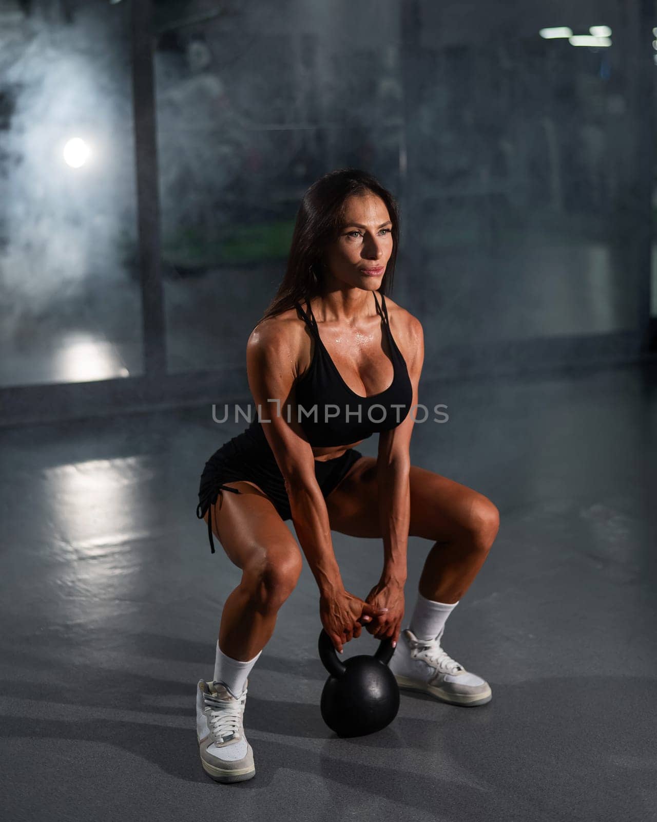 Caucasian woman squats with a kettlebell in the gym. Vertical photo