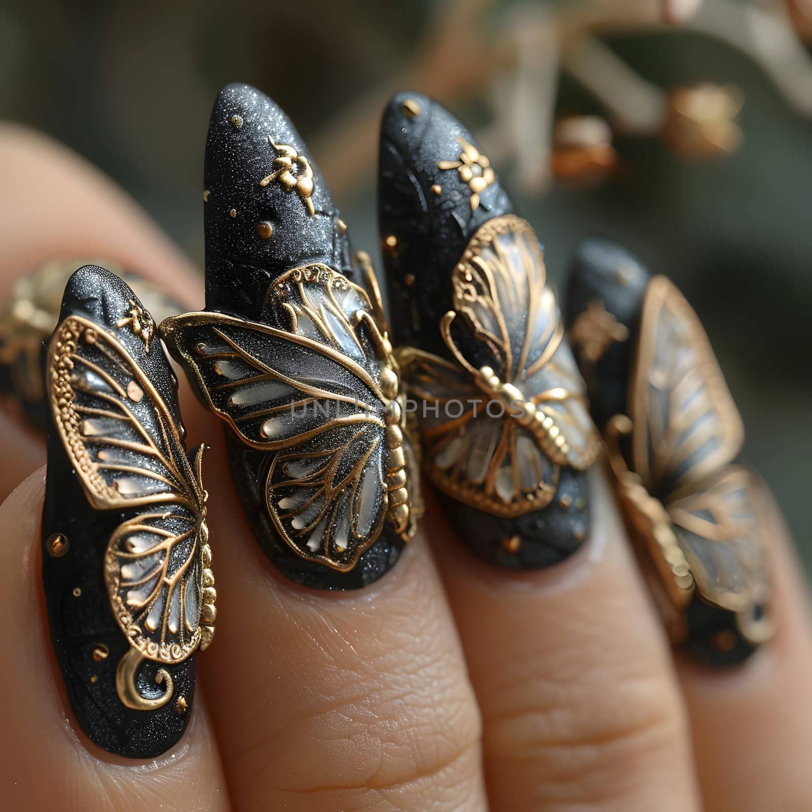 The womans fingers are adorned with intricate black and gold butterfly nail art, resembling tiny pieces of jewellery made from metal, creating a stunning fashion accessory