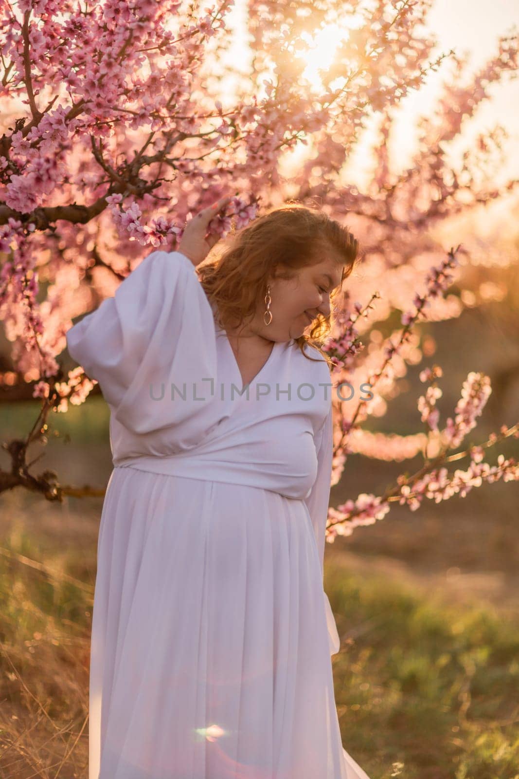 Woman blooming peach orchard. Against the backdrop of a picturesque peach orchard, a woman in a long white dress enjoys a peaceful walk in the park, surrounded by the beauty of nature. by Matiunina