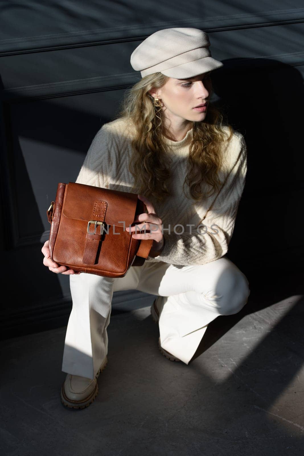 Studio portrait of beautiful woman with a curly blond hair holding brown bag, posing on gray background. by Ashtray25