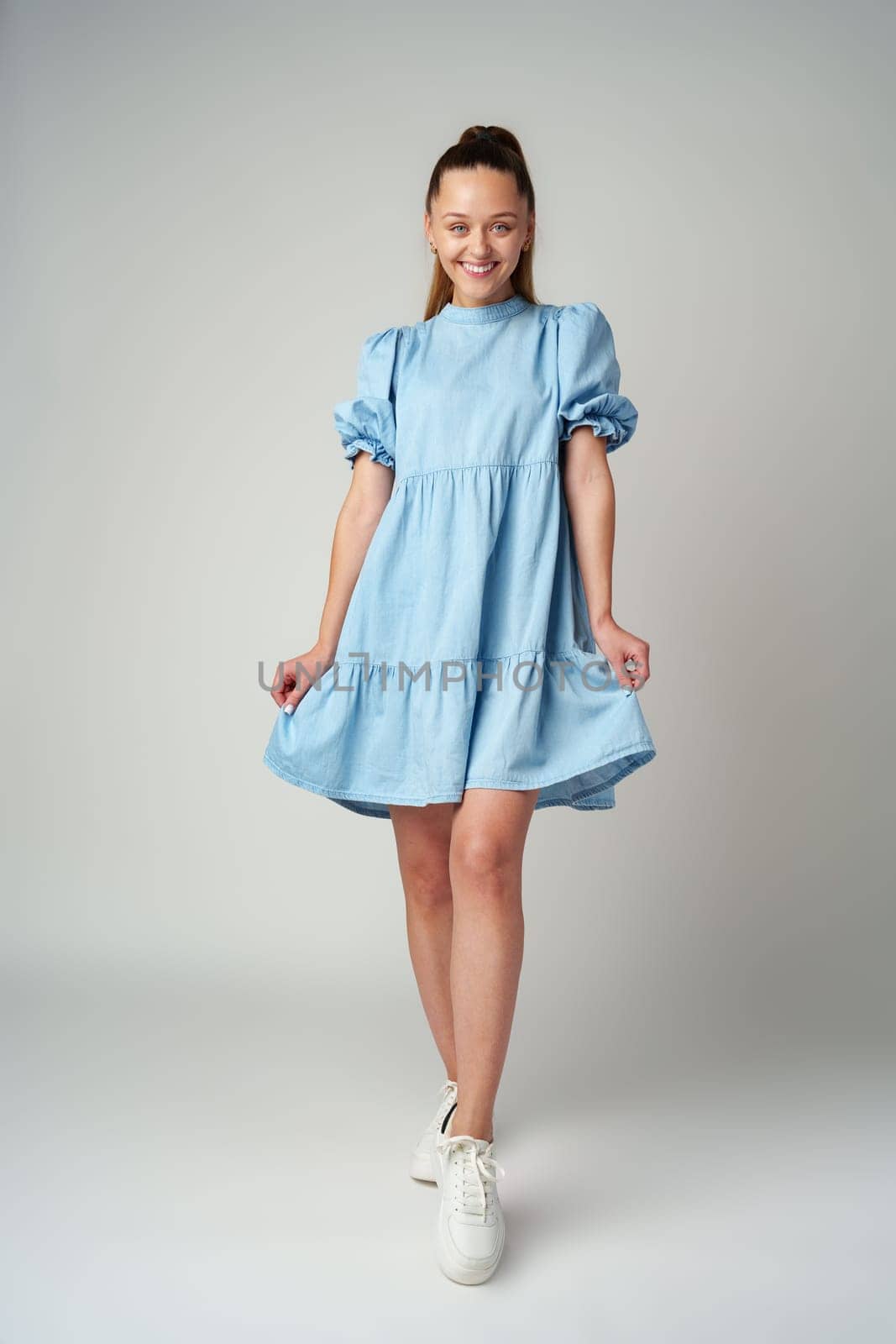Young happy smiling woman in a light blue dress on a gray background by Fabrikasimf