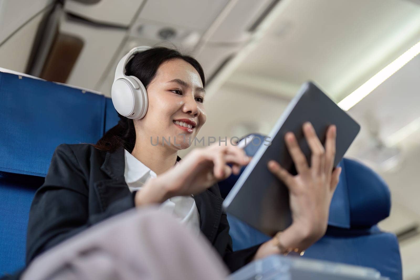 Asian young woman wearing headphone listen to music at first class on airplane during flight, Traveling and Business concept by nateemee