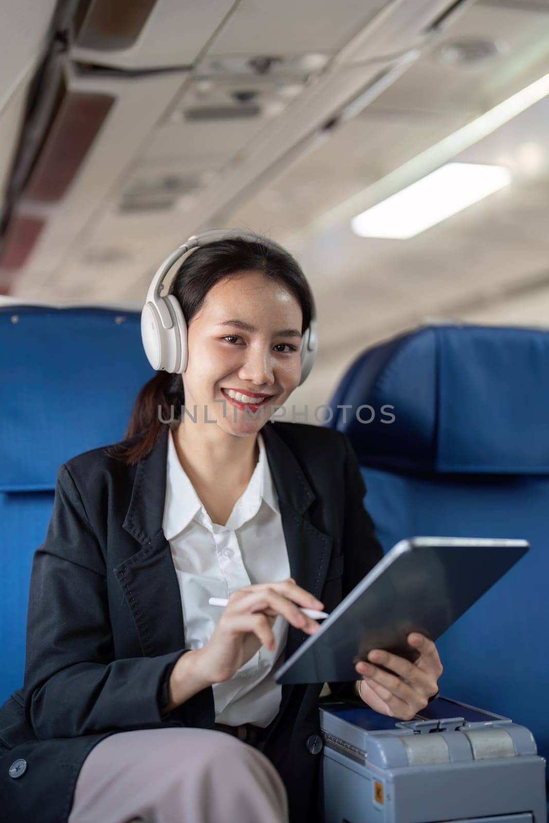Asian young woman wearing headphone listen to music at first class on airplane during flight, Traveling and Business concept.