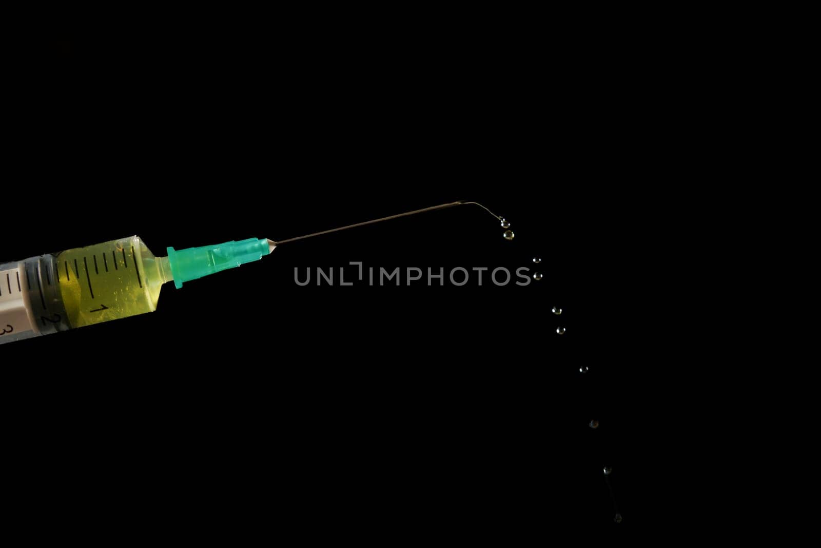 syringe with needle, a row of drops of yellow liquid coming out, isolated on black background and copy space