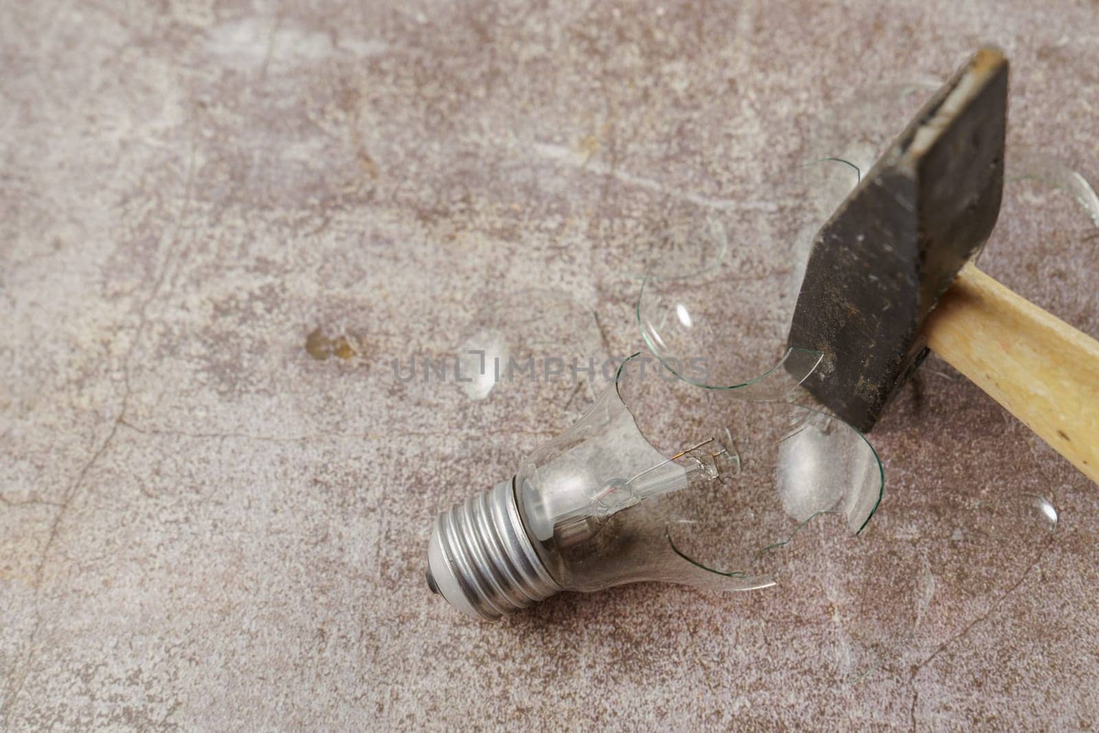 top view of a broken light bulb with a hammer on concrete floor
