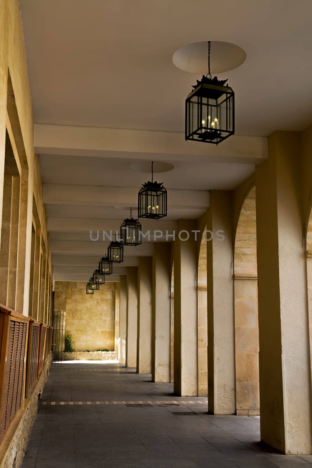 hallway with arches and lighted ceiling lamps with sunlight in the background