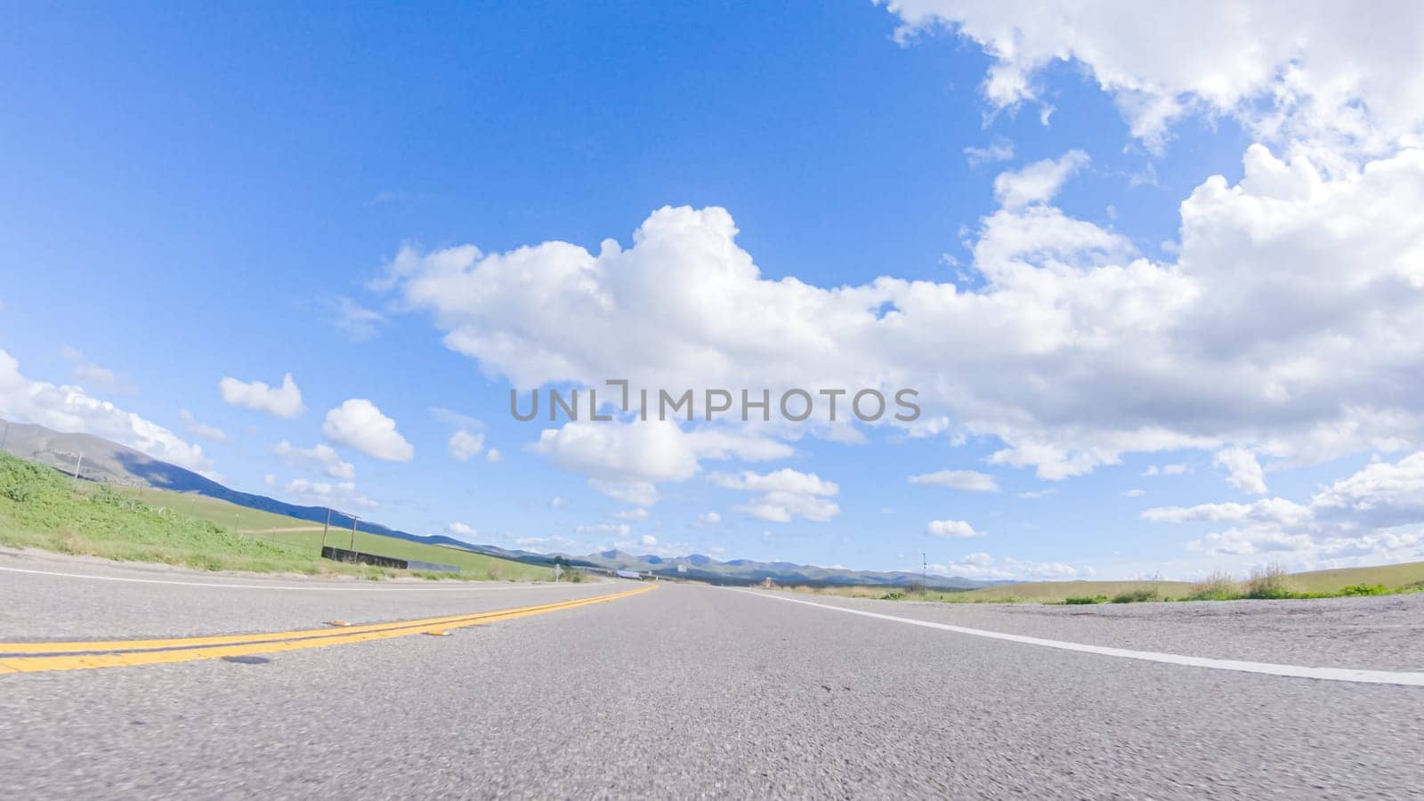 On a clear winter day, a car smoothly travels along Highway 101 near Santa Maria, California, under a brilliant blue sky, surrounded by a blend of greenery and golden hues.