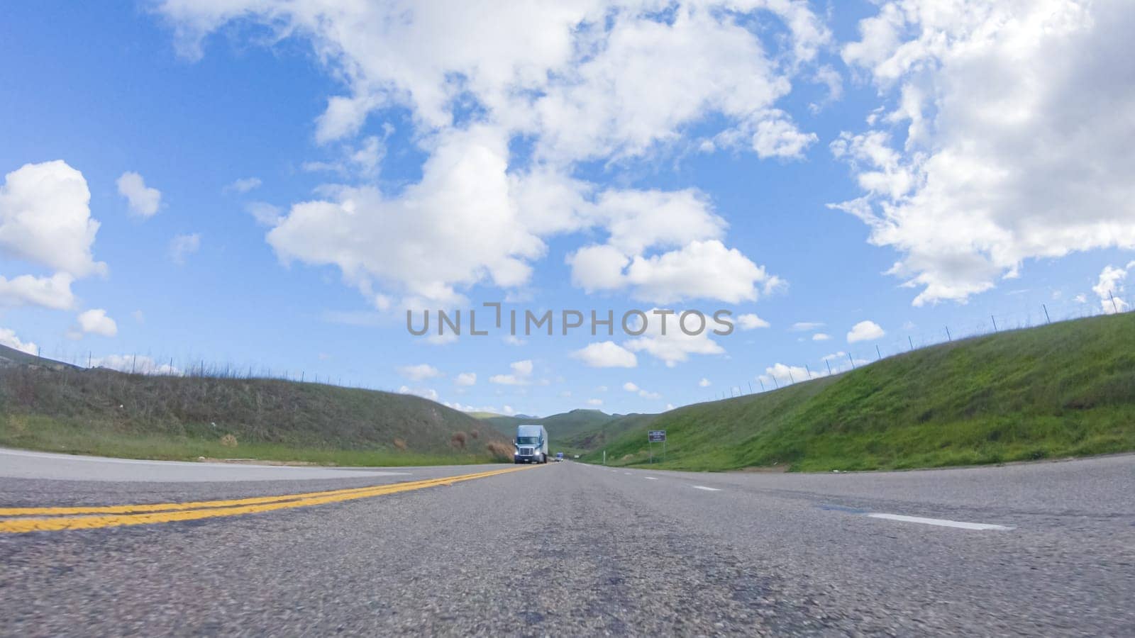 On a clear winter day, a car smoothly travels along Highway 101 near Santa Maria, California, under a brilliant blue sky, surrounded by a blend of greenery and golden hues.