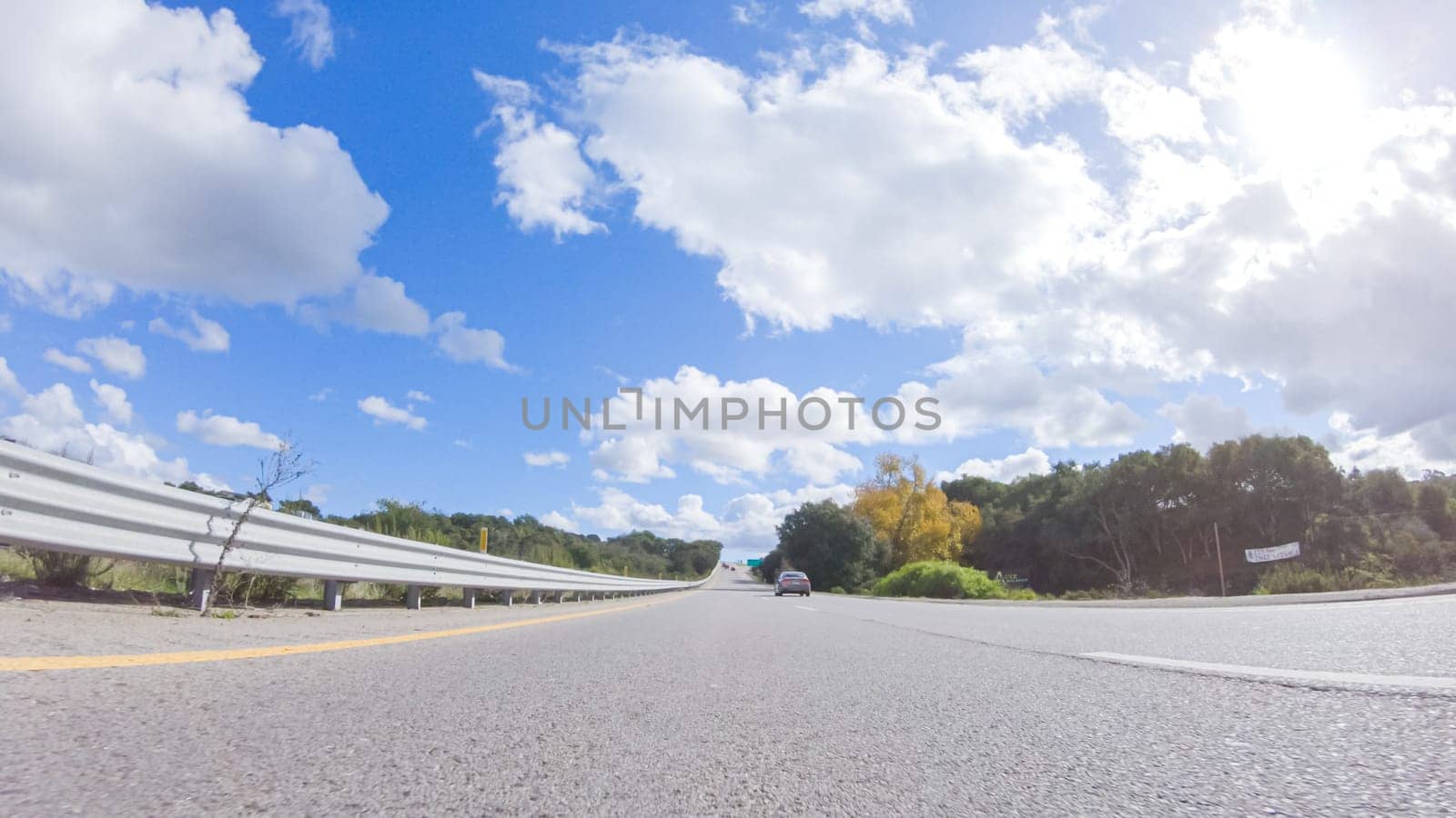 On a clear winter day, a car smoothly travels along Highway 101 near Santa Maria, California, under a brilliant blue sky, surrounded by a blend of greenery and golden hues.