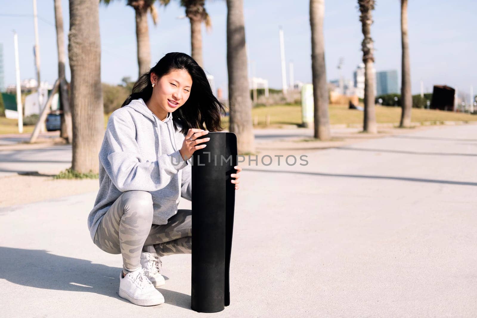 young asian woman dressed in sportswear preparing her mat for a yoga session outdoors, healthy and active lifestyle concept, copy space for text