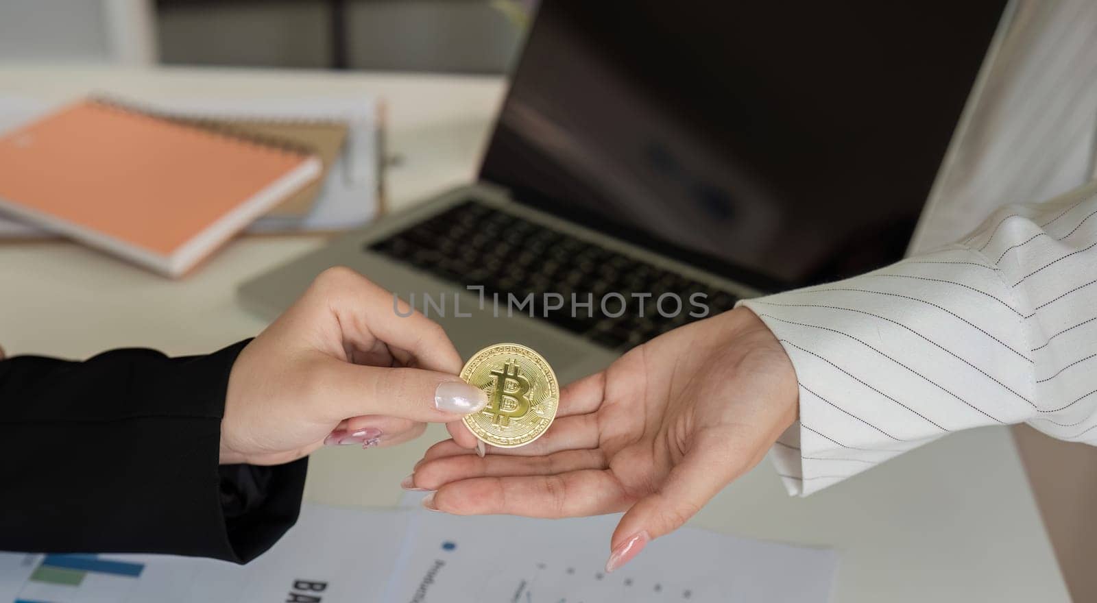 Two businesswomen hand each other cryptocurrency coins. Cryptocurrency exchange concept by wichayada