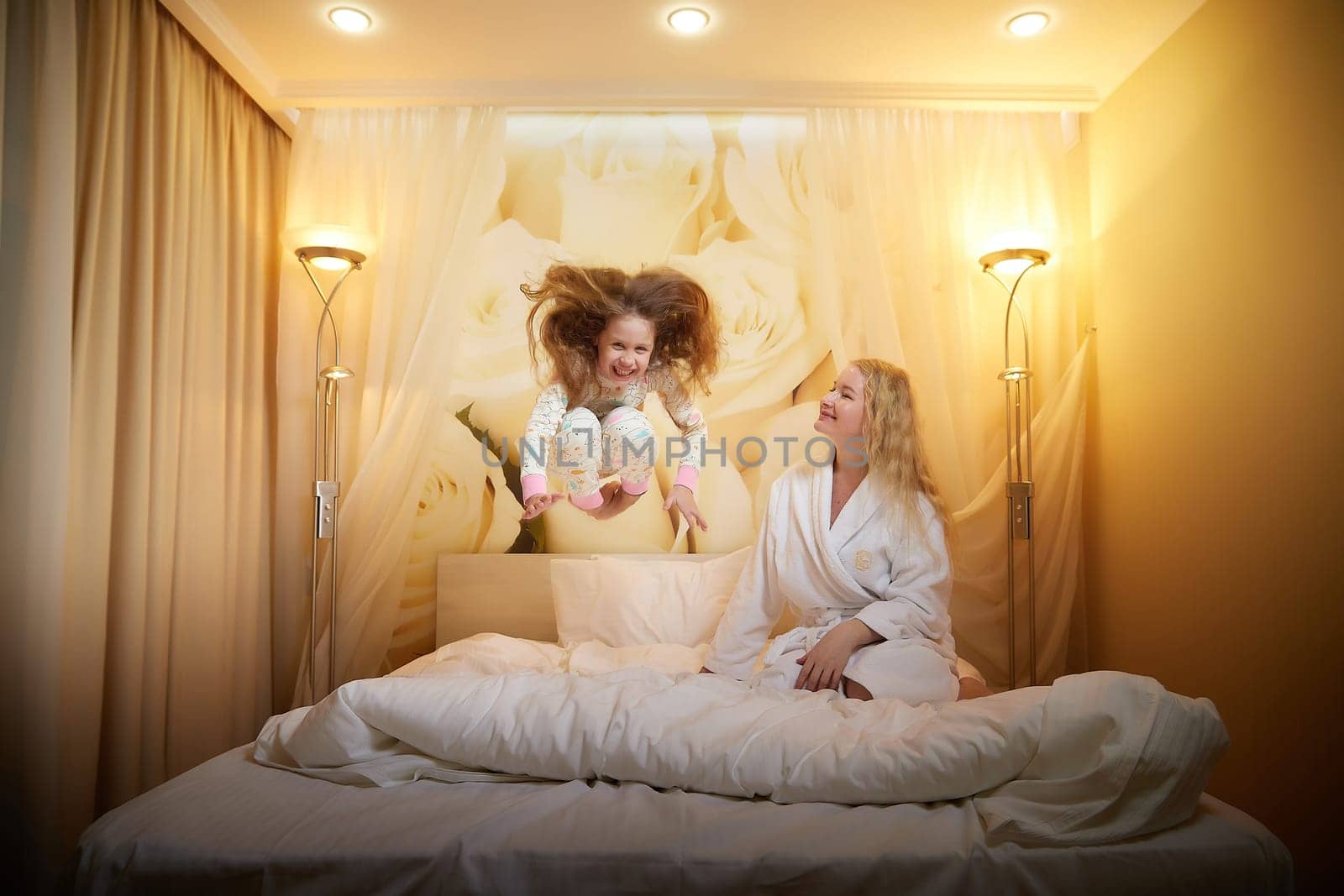 Mother and daughter happily relax and fun together on bed in bedroom. The concept of tenderness between mom and girl