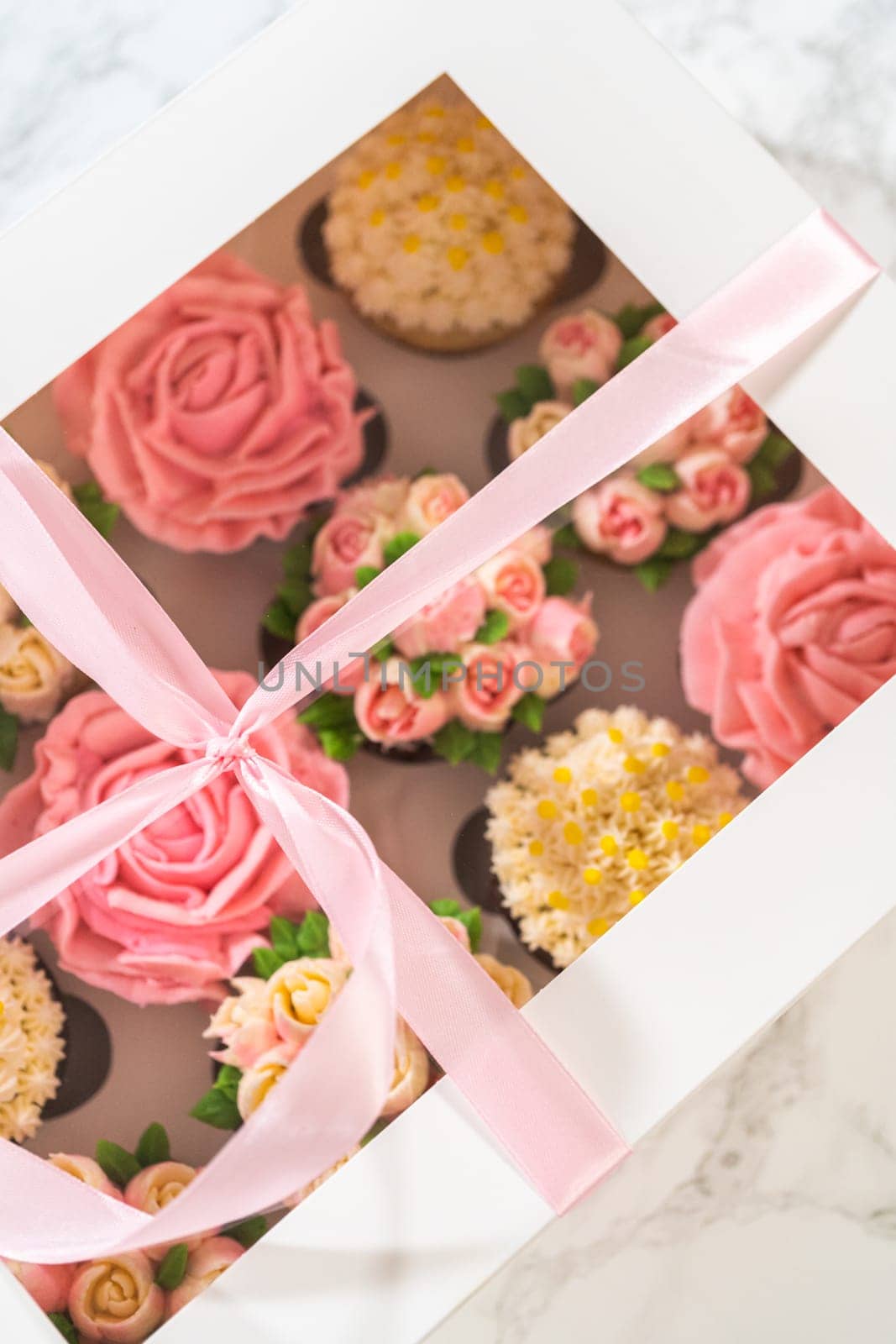 Encased in a pristine white paper cupcake box, each gourmet cupcake is a work of art, adorned with buttercream frosting flowers beautifully designed to resemble vibrant roses and tulips.