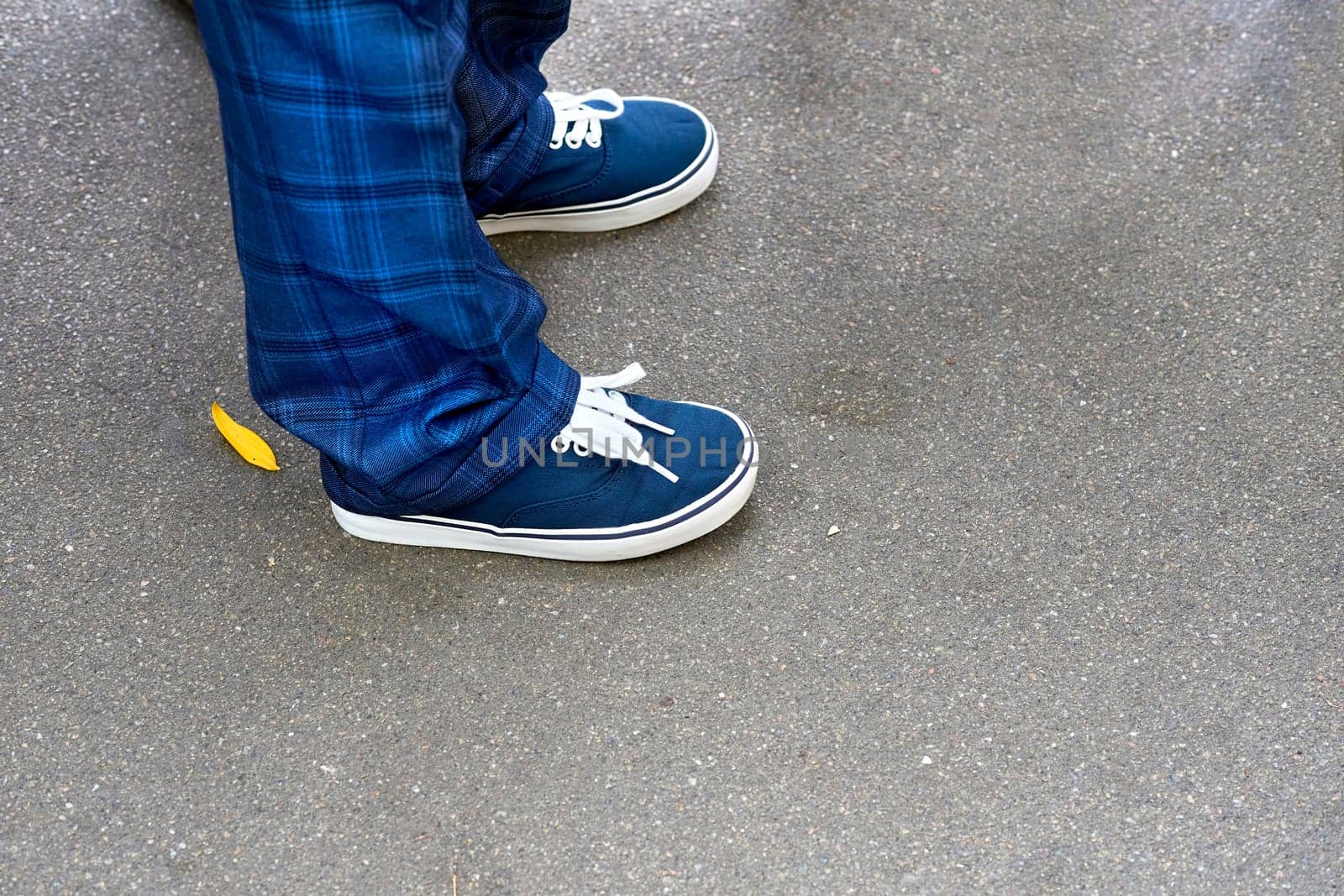 Legs of a schoolboy in blue plaid trousers and sneakers with laces by jovani68