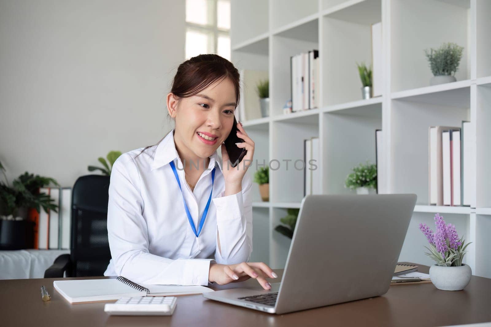 Young businesswoman talking on the phone in an online business meeting using a laptop in a modern home office..
