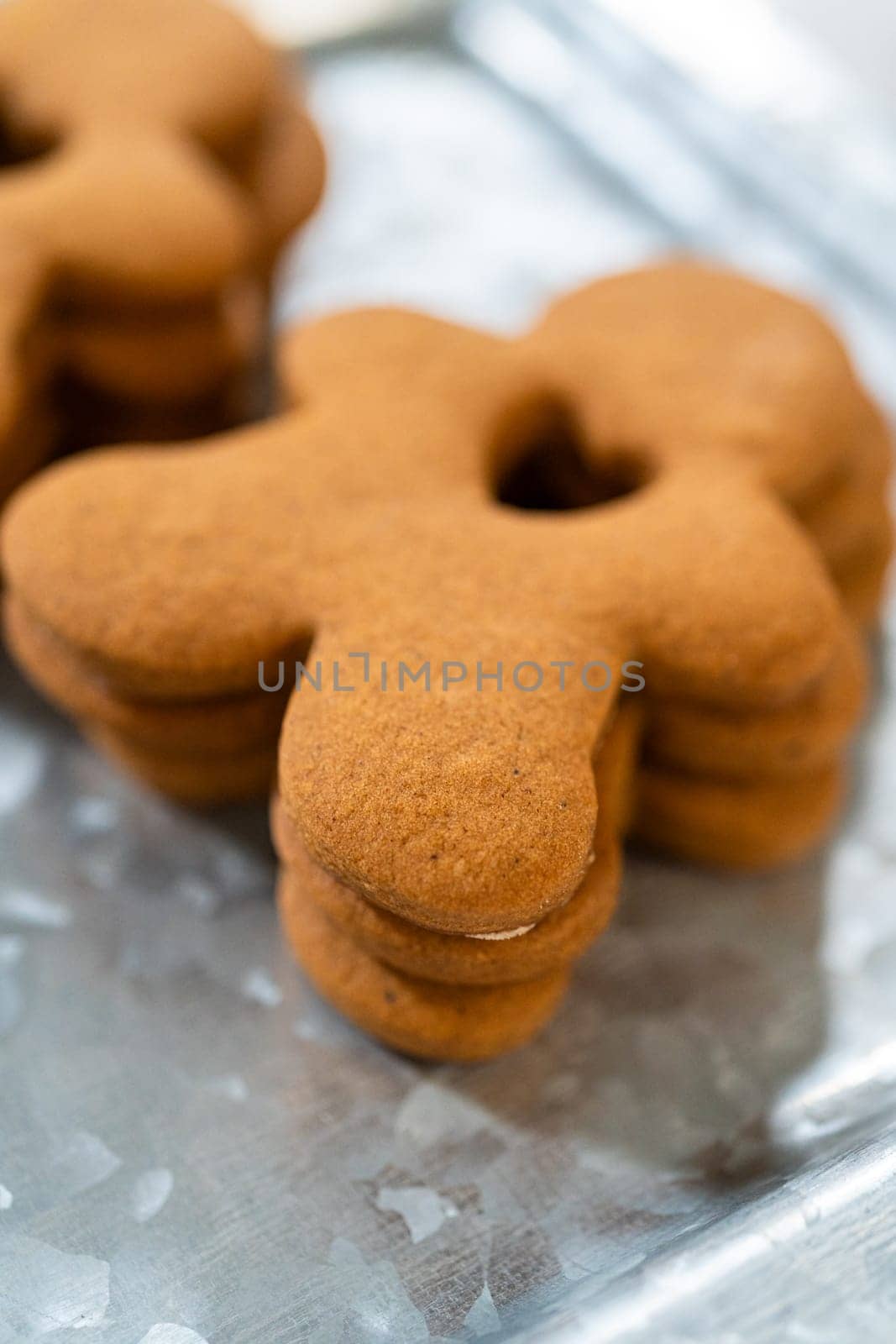 Gingerbread cookies, including a gingerbread man with a heart-shaped cutout, rest on a rustic metal tray against a marble countertop.