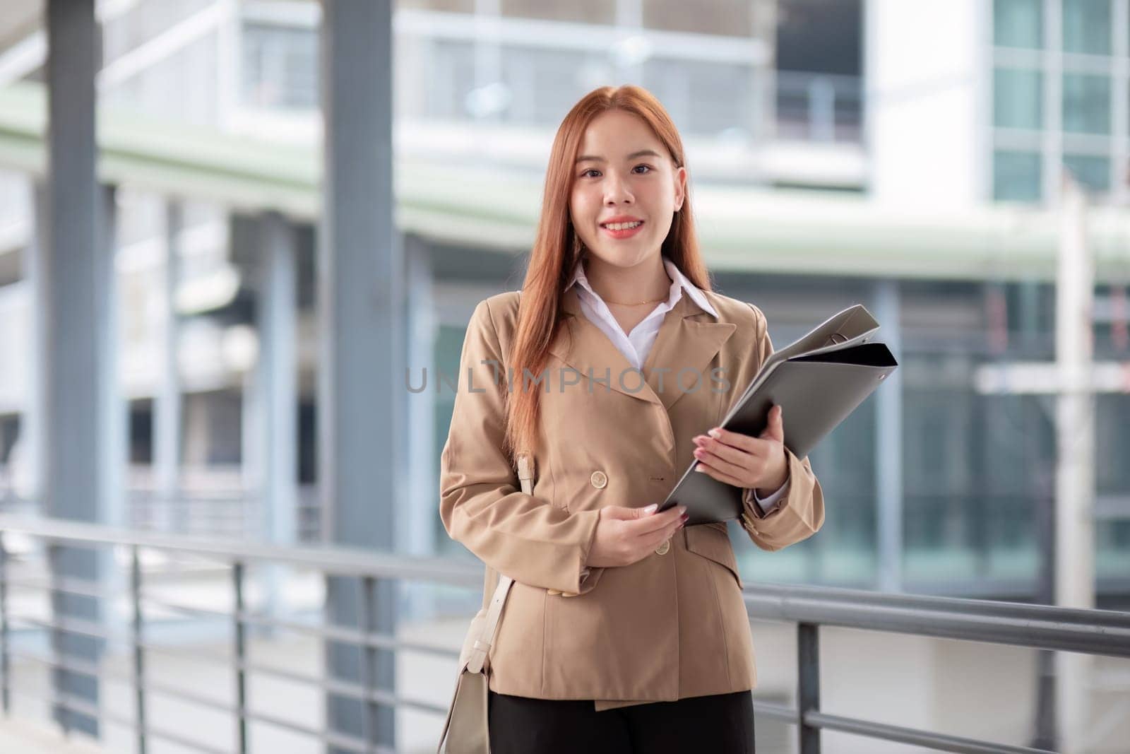 Young beautiful successful business woman outside office building, successful Asian woman smiling standing with documents.