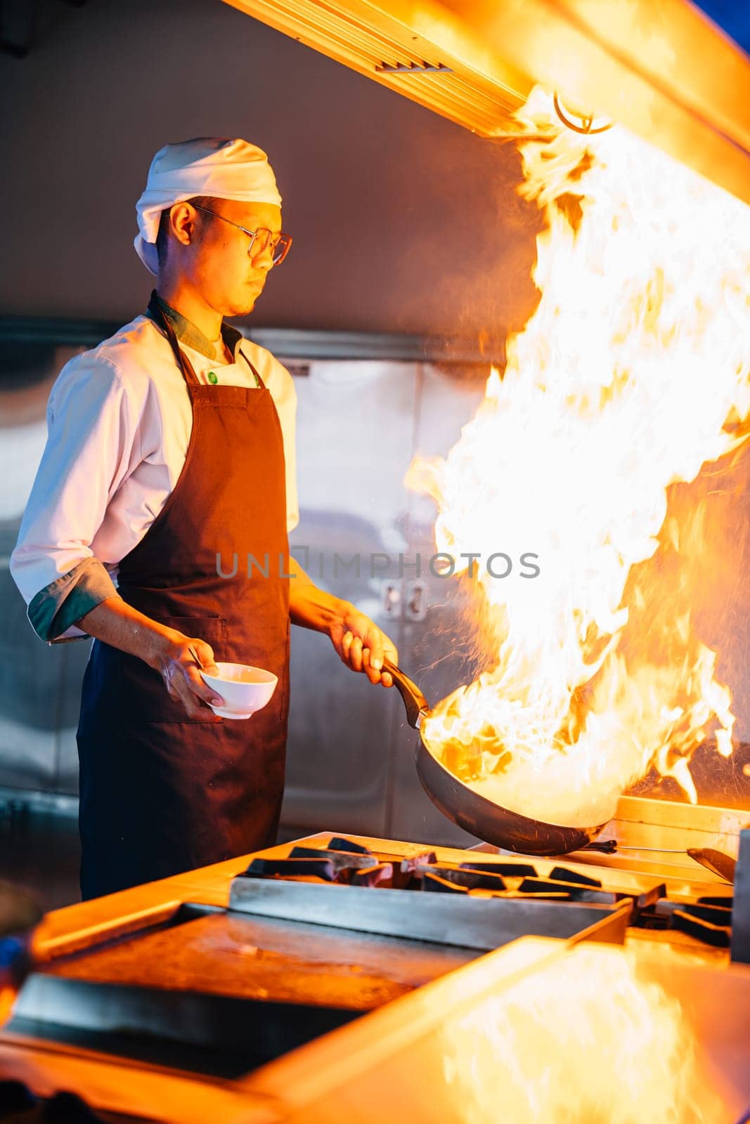 Chef hands with wok and fire. Closeup of chef cooking food with flames in professional kitchen. Expertise at work busy cooking handling flames in a modern setting. cook food with fire