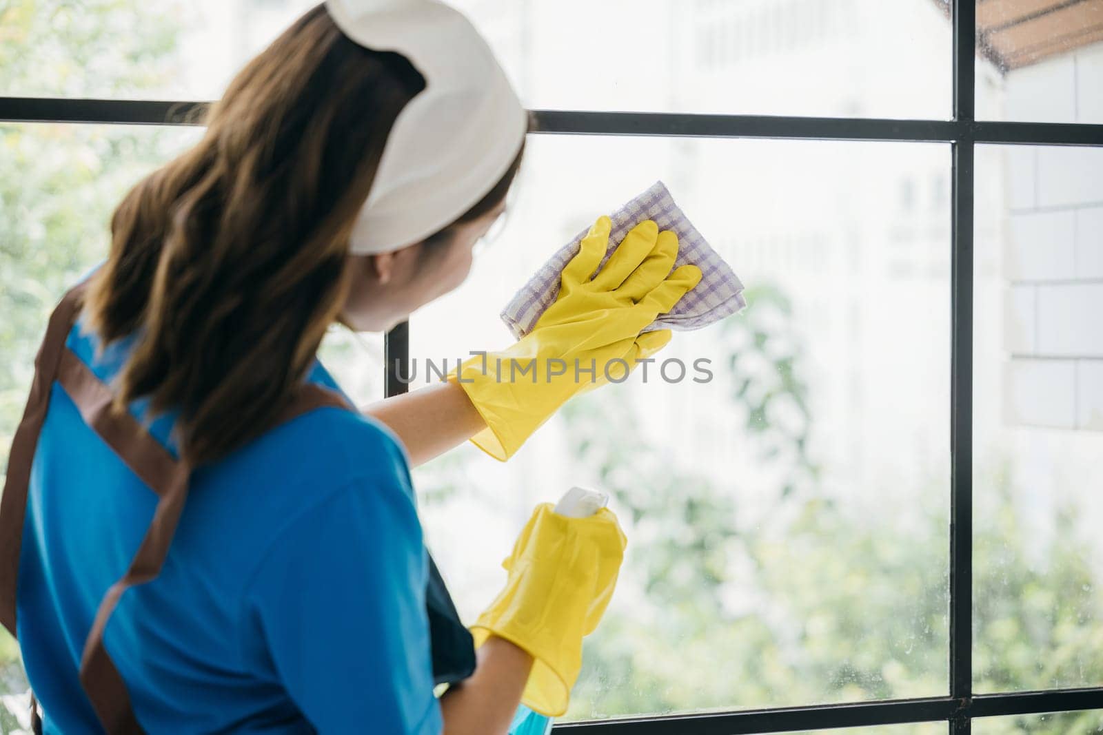 With a cheerful demeanor a young woman diligently cleans office windows using spray and cloth. Her housework emphasizes purity hygiene and transparent cleanliness.
