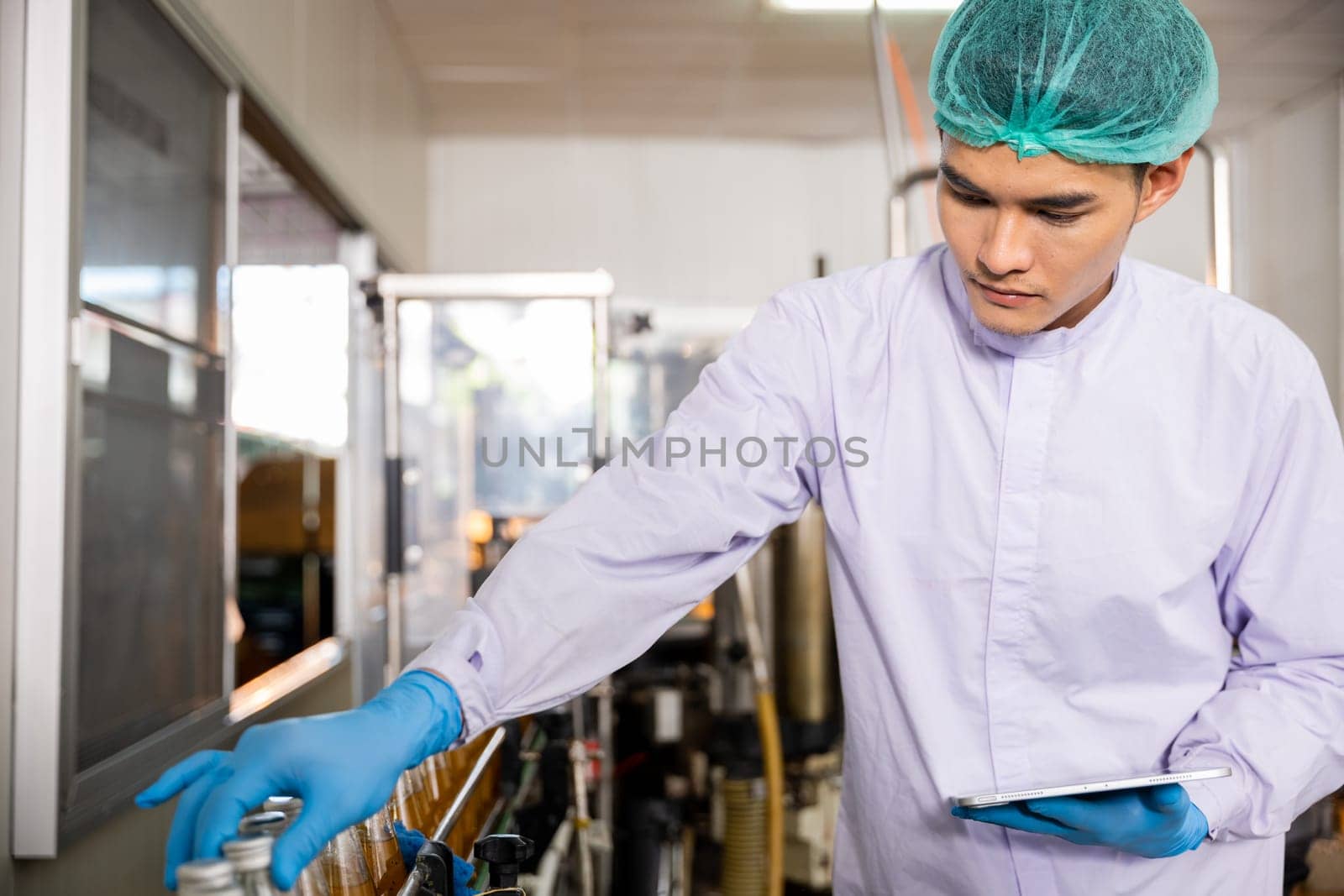 Inspecting the beverage bottling factory a quality control officer ensures line efficiency with a tablet. The machinery engineer checks and maintains machines for basil or chia seed bottle production.