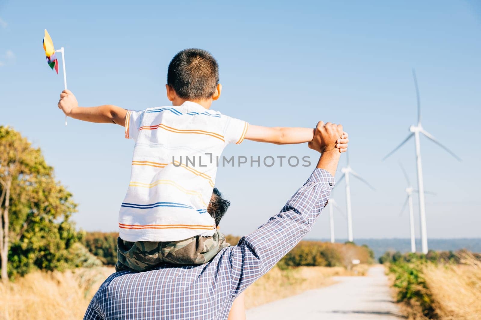Dad carries daughter with pinwheel smiling. Family fun near windmills showcases global innovation in renewable energy. Bonding joy and happiness in the community. Father Day Concept