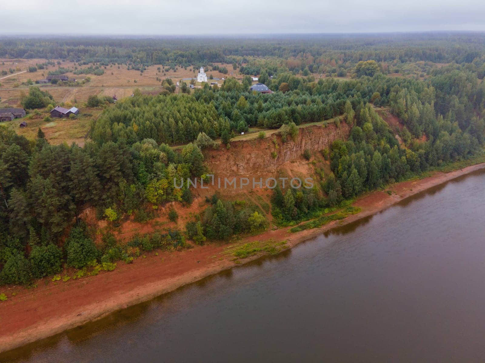 Drone view of village with river against shore with lush green trees on mount in region of Kirov Russia